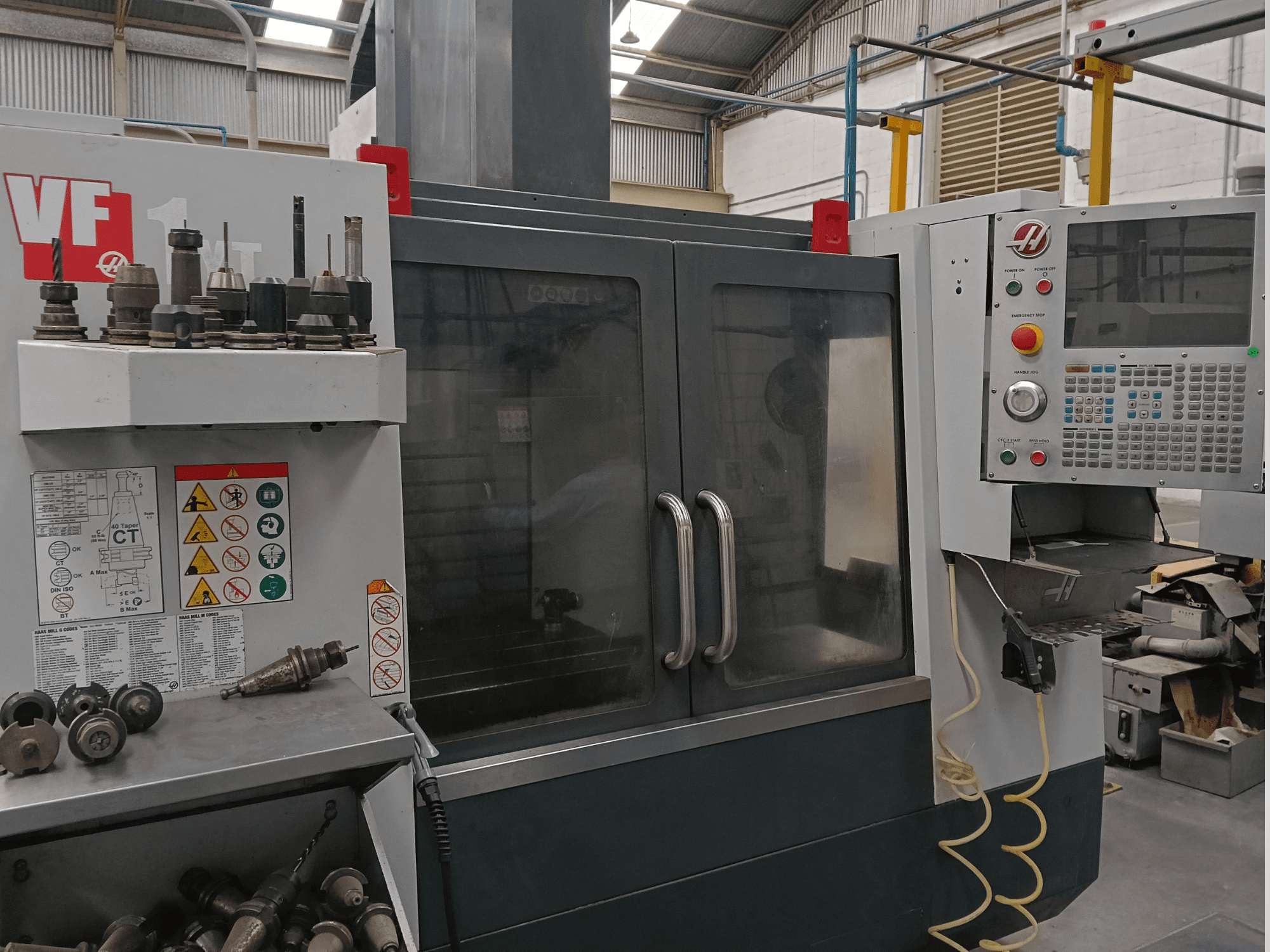 Вертикальный обрабатывающий центр HAAS VF-1YT-3 в виде спереди, на котором видны органы управления, держатели инструментов и защитные наклейки.