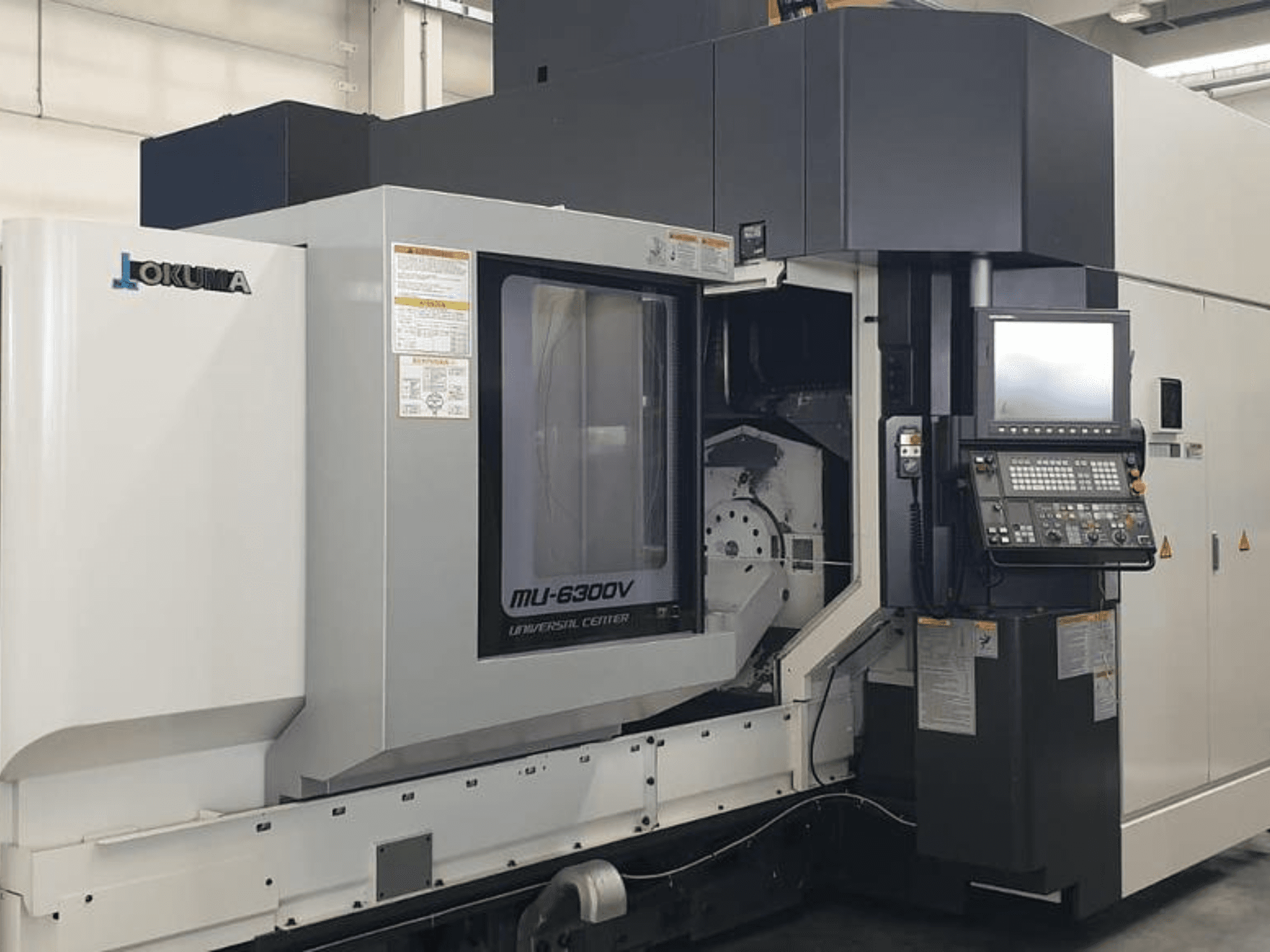 Вертикальный обрабатывающий центр Okuma MU 6300 V, вид спереди, демонстрирующий панель управления и детали зоны обработки.
