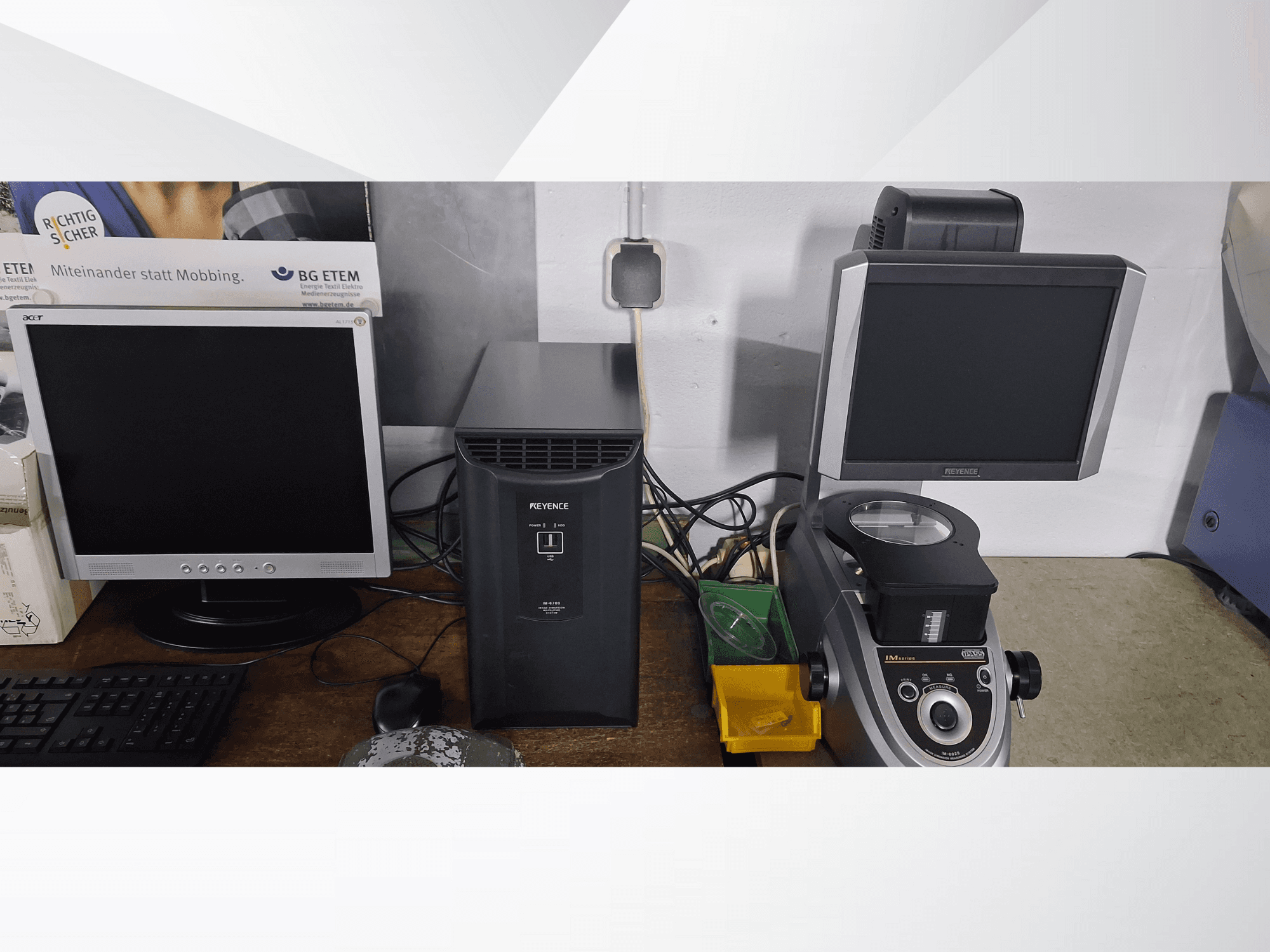 Два компьютерных монитора, один Acer, другой Keyence, рядом с черным устройством и микроскопом, вид спереди.