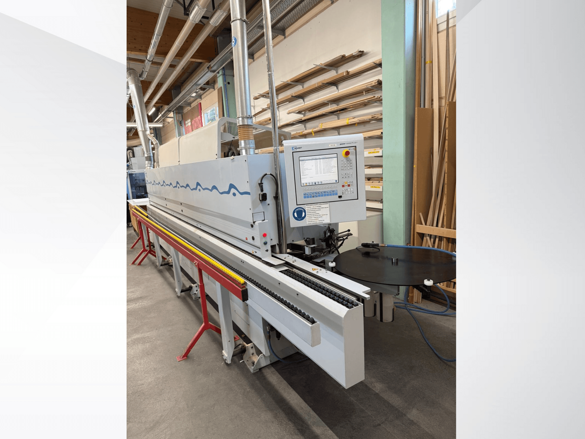 Вид спереди автоматического кромкооблицовочного станка HolzHer с панелью управления, системой транспортировки и круглым опорным столом.