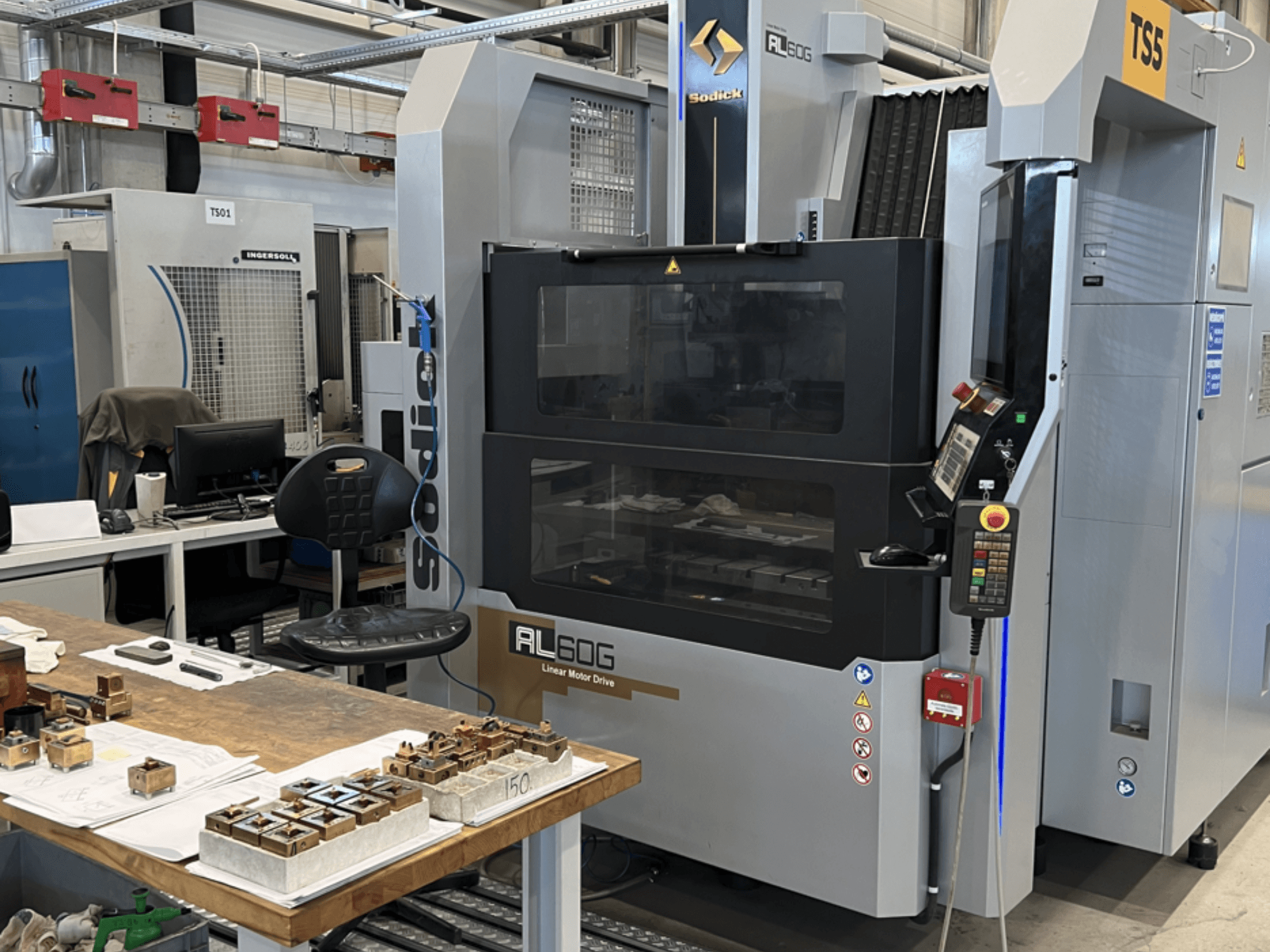 Sodick AL60G Die-Sinking EDM Machine; вид спереди, показывающий элементы управления, окно и рабочую область с различными металлическими деталями.