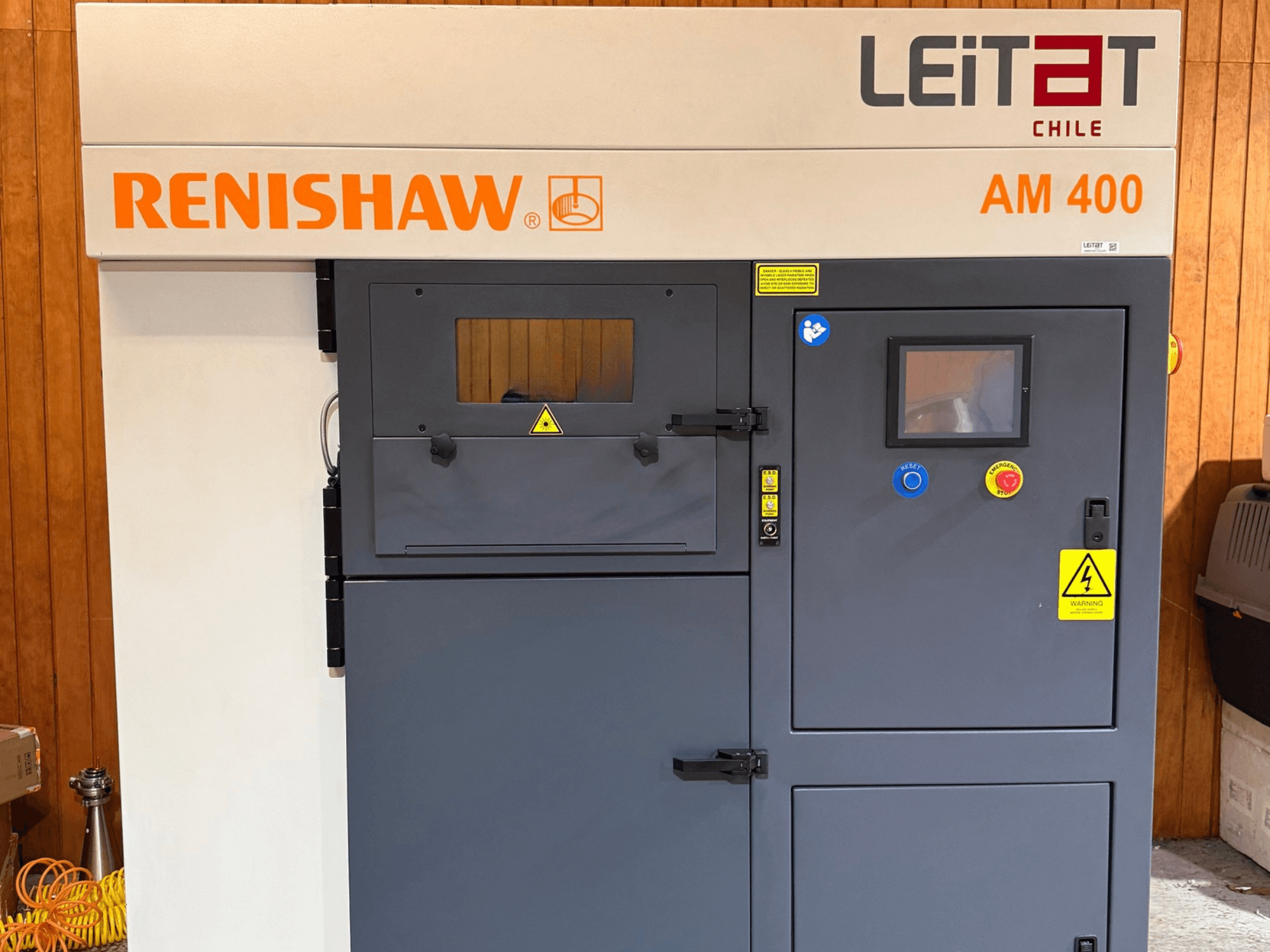Вид спереди на 3D-принтер RENISHAW AM400 для печати из металла с панелью управления, предупреждающими надписями и отверстиями для доступа при техническом обслуживании.