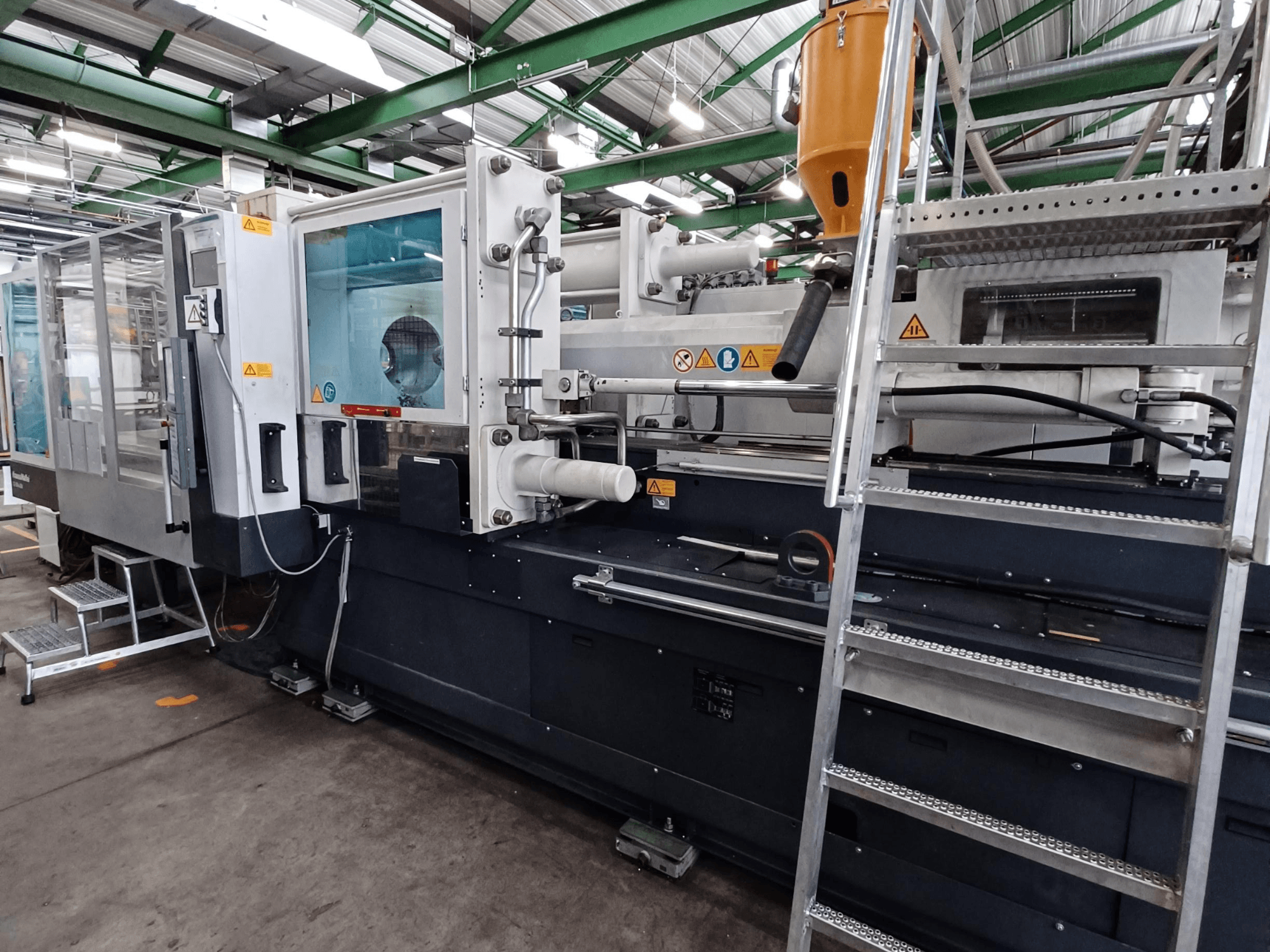 Промышленный термопластавтомат с четким видом спереди, на котором видны маркировка бренда, панель управления и бункер для материала.