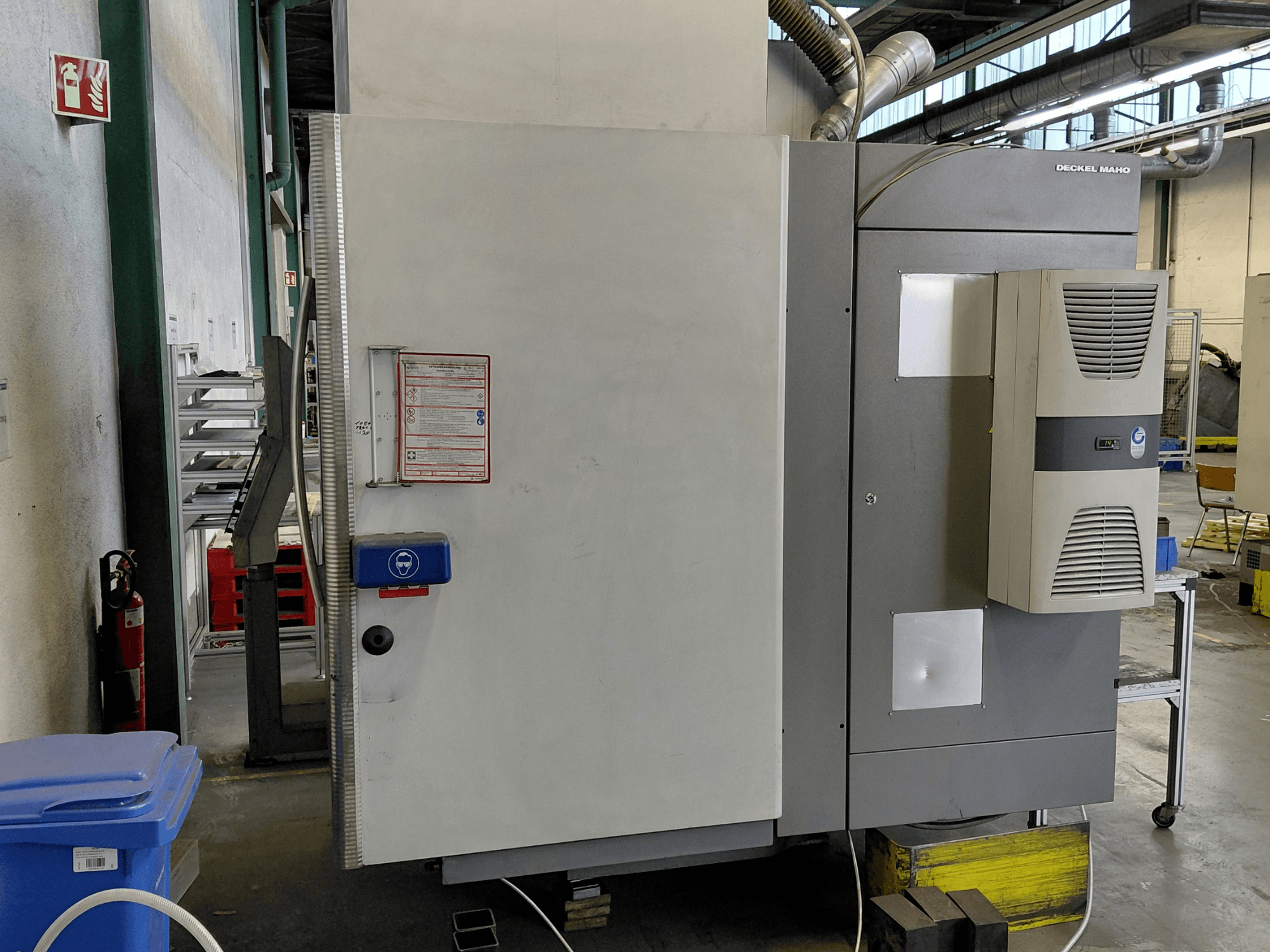 Вид сбоку вертикального обрабатывающего центра DECKEL MAHO DMC 635 V с панелью управления и наклейками безопасности.