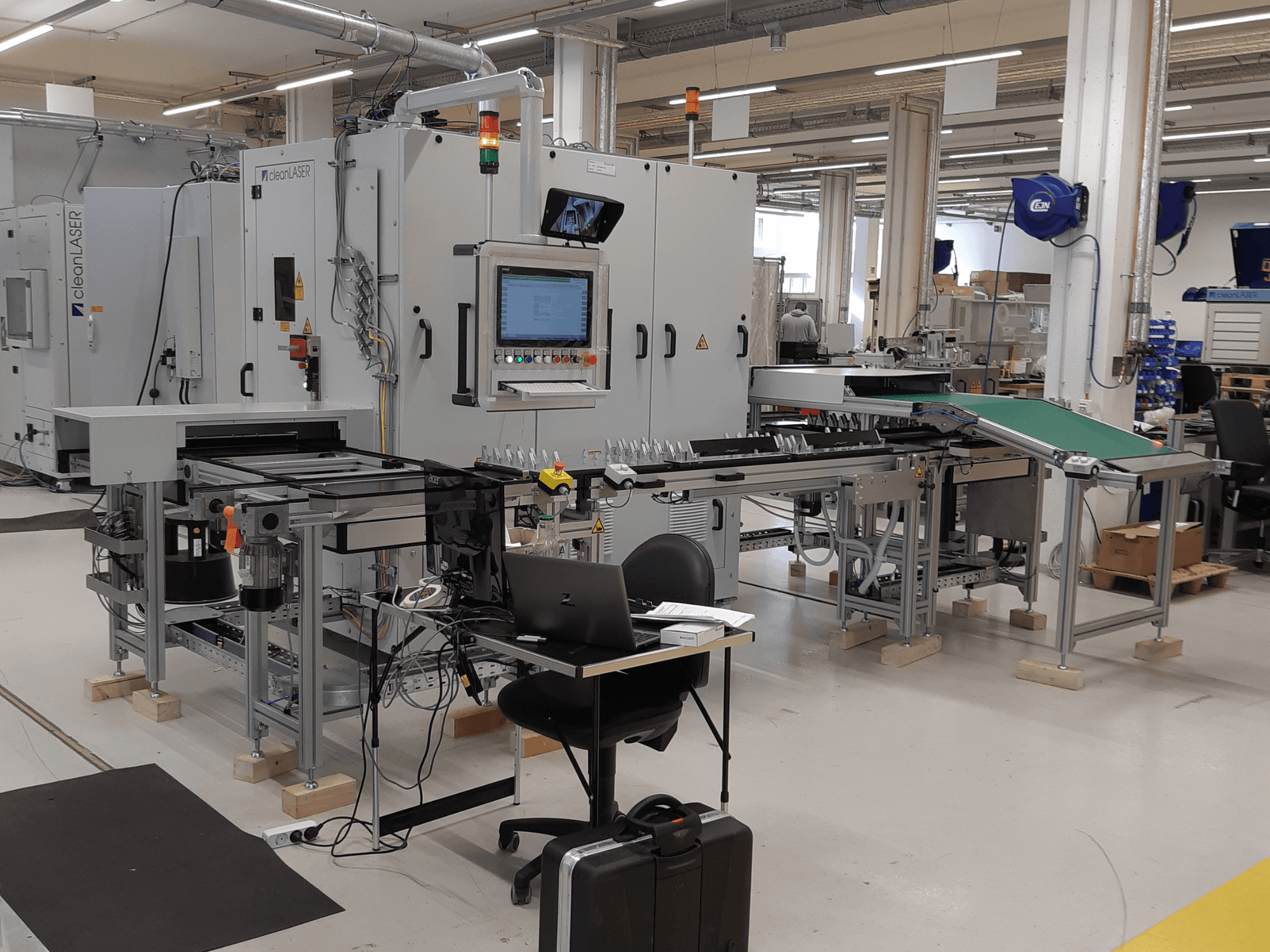 Станк CLEAN LASER clean CELL 3220 CL600, вид спереди, с панелью управления, конвейером и рабочей зоной, расположенный в цехе.