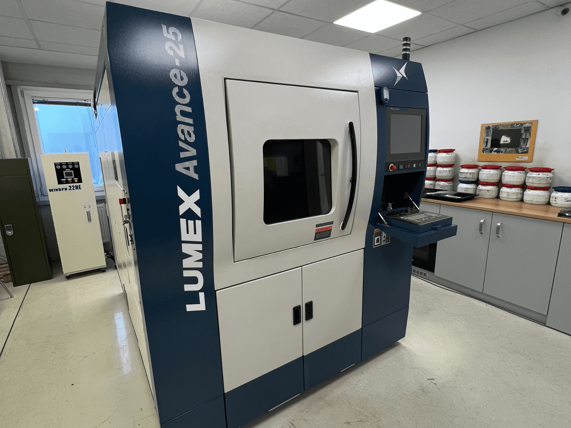 3D-принтер LUMEX Avance-25 в лабораторных условиях, вид спереди. Панель управления с экраном и кнопками, оборудование на заднем плане.