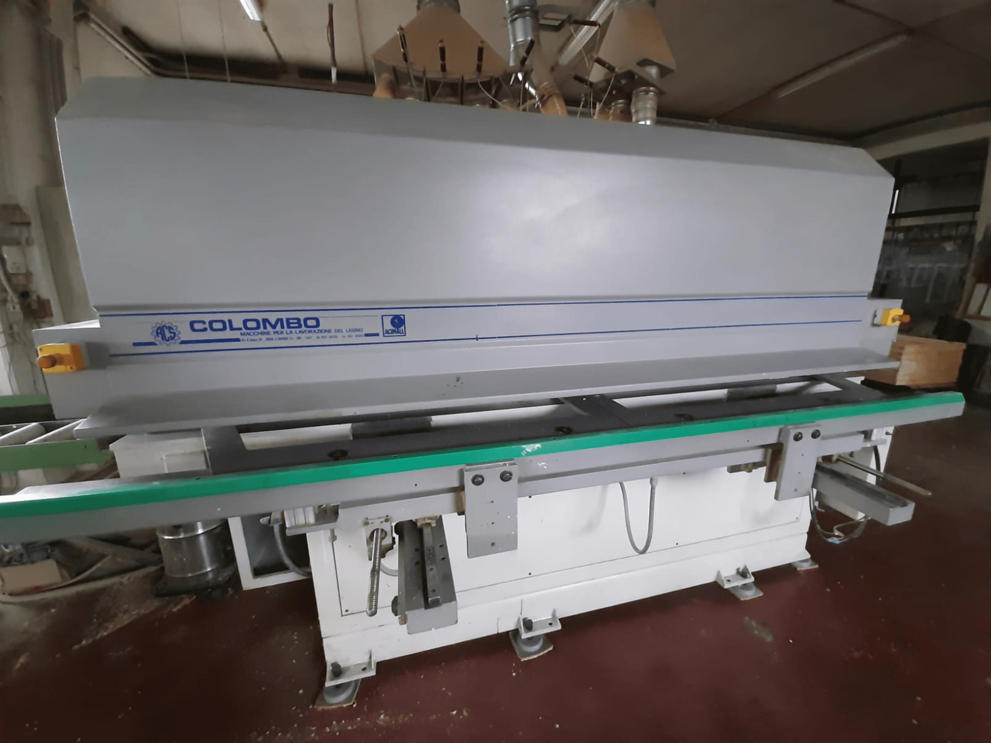 Деревообрабатывающий станок Colombo, вид спереди, с длинным зеленым столом, кнопками управления и серым корпусом с синими акцентами.