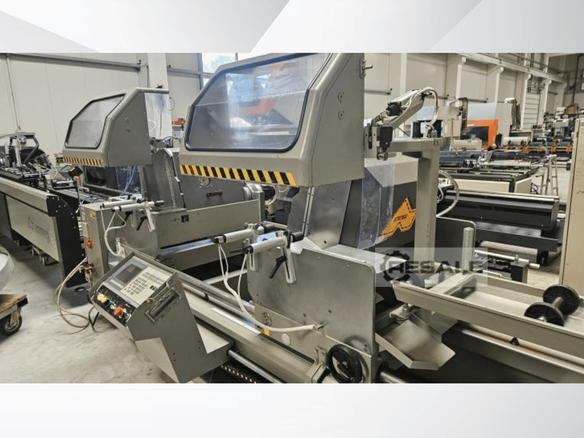 Двухпильные станки на заводе; вид спереди, на котором видны панель управления, стеклянные крышки и режущие элементы.