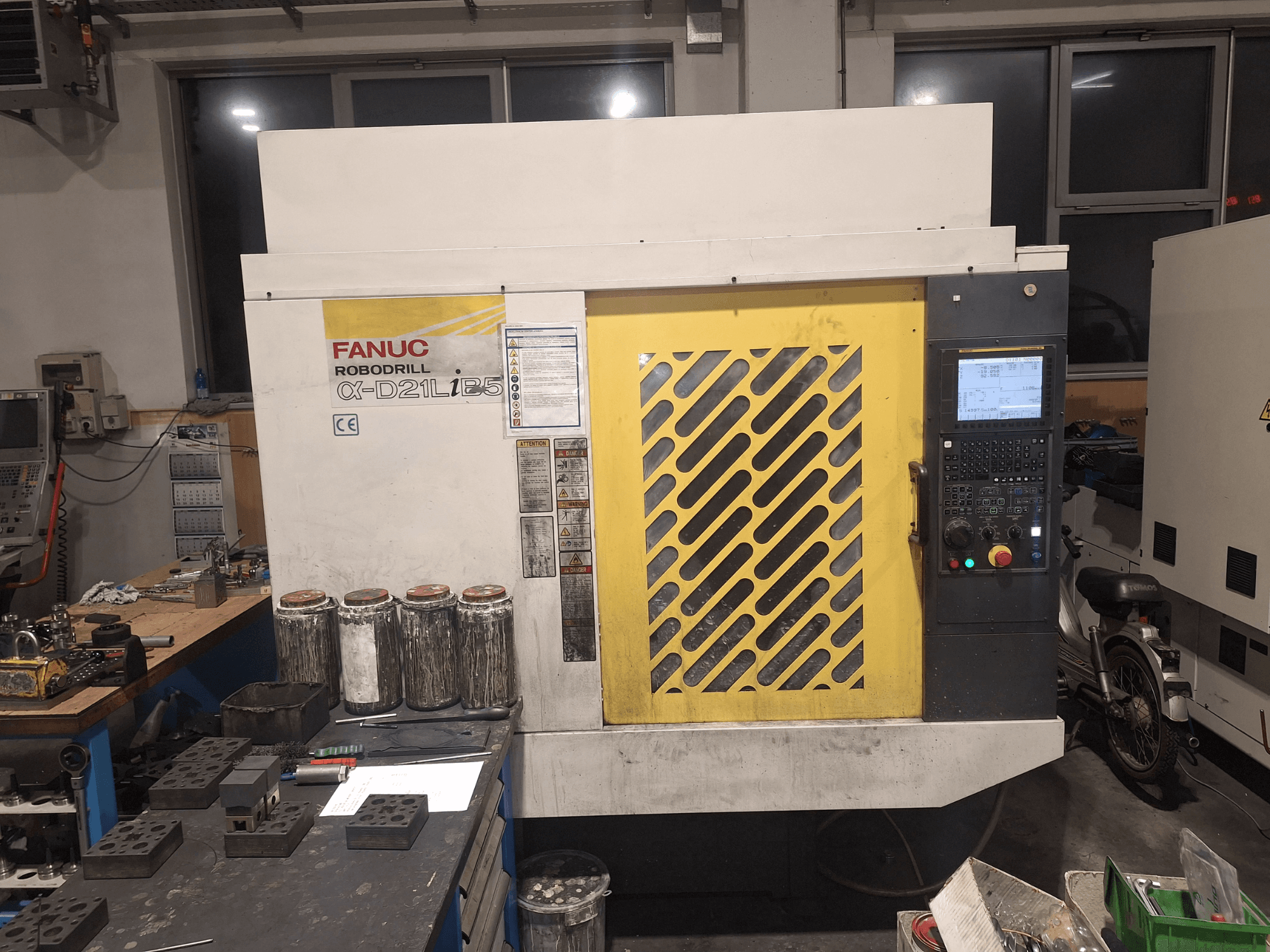 Вид спереди на FANUC Robodrill α-D21LiB5, на котором видны панель управления, желтая решетка и расположенные рядом инструменты на верстаке.