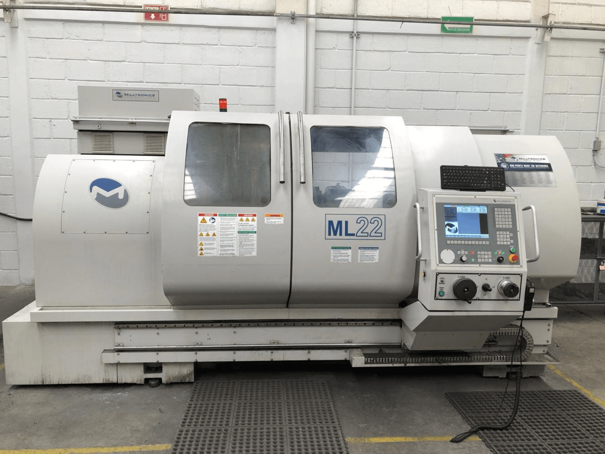 Вертикальный обрабатывающий центр MILLTRONICS RH 20, вид спереди, на котором изображена панель управления, логотип бренда и наклейки безопасности на станке.