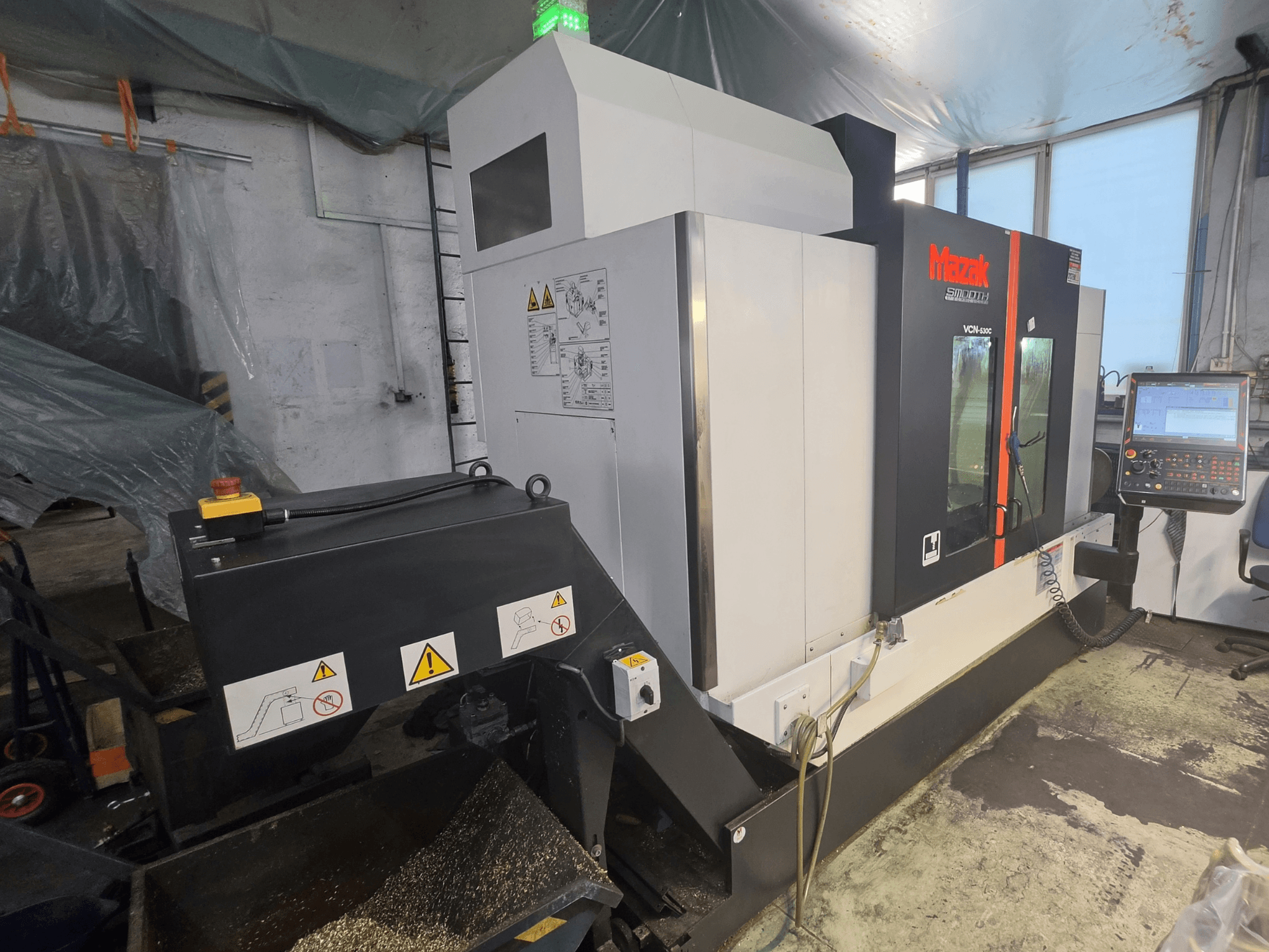 Вертикальный обрабатывающий центр Mazak VCN-530C, вид спереди, на котором видны панель управления, цепь инструментов и индикаторы рабочего состояния.