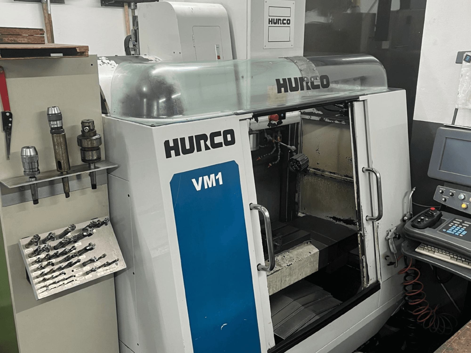 Вид спереди вертикального обрабатывающего центра Hurco VM1 с прозрачной крышкой, панелью управления и установленными инструментами.