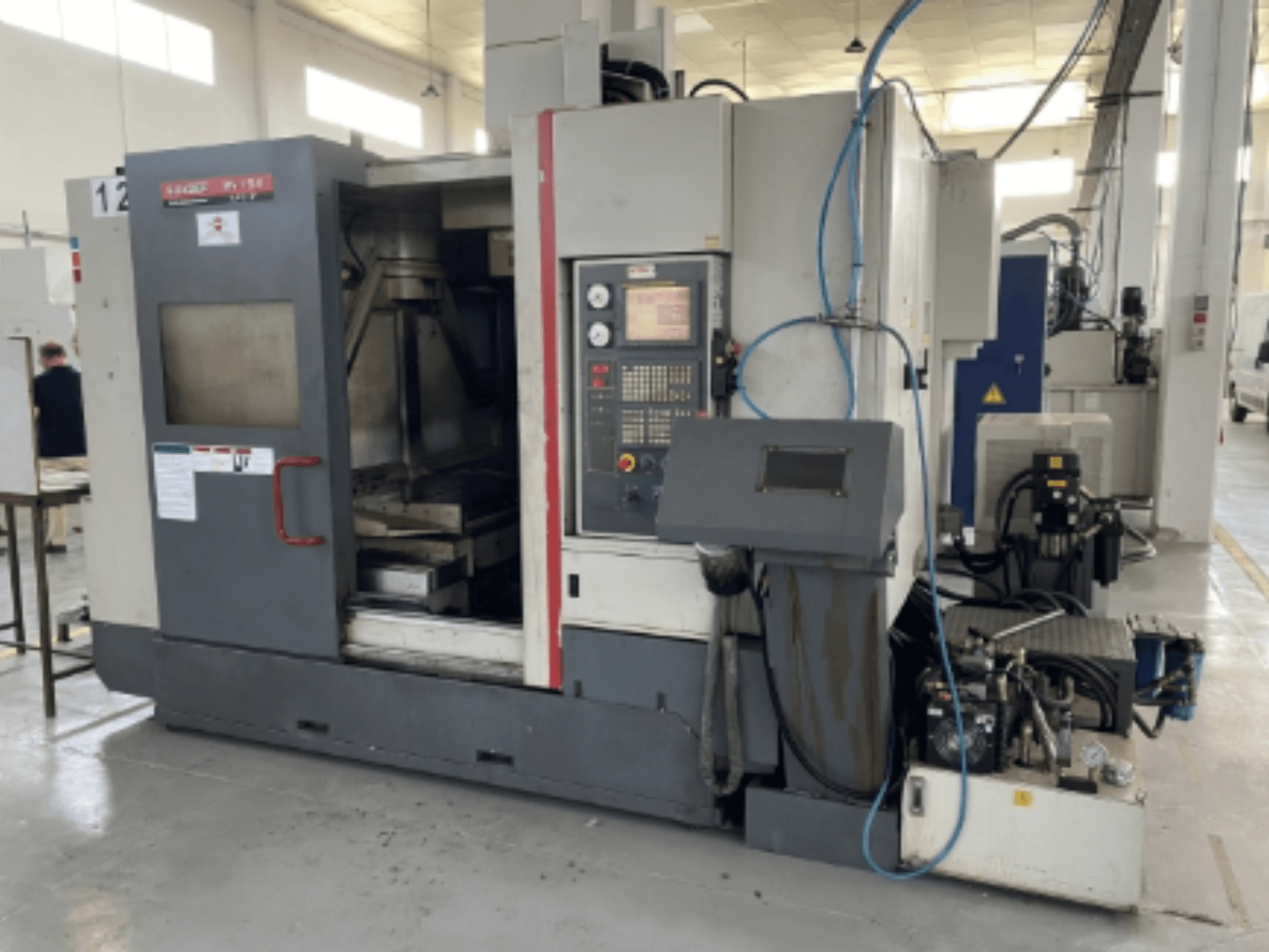 Вертикальный обрабатывающий центр Quaser MV154APC-912, вид спереди с изображением панели управления, открытой двери и компонентов станка.