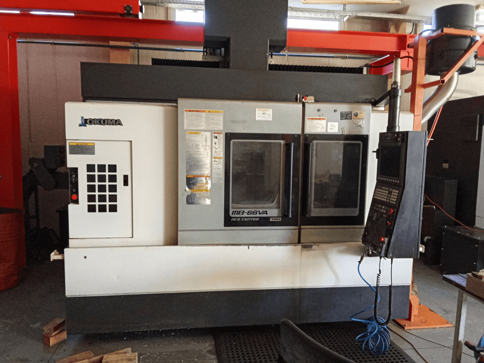 Вертикальный обрабатывающий центр Okuma MB-66VA, вид спереди с панелью управления и двумя смотровыми окнами для доступа к инструментам.