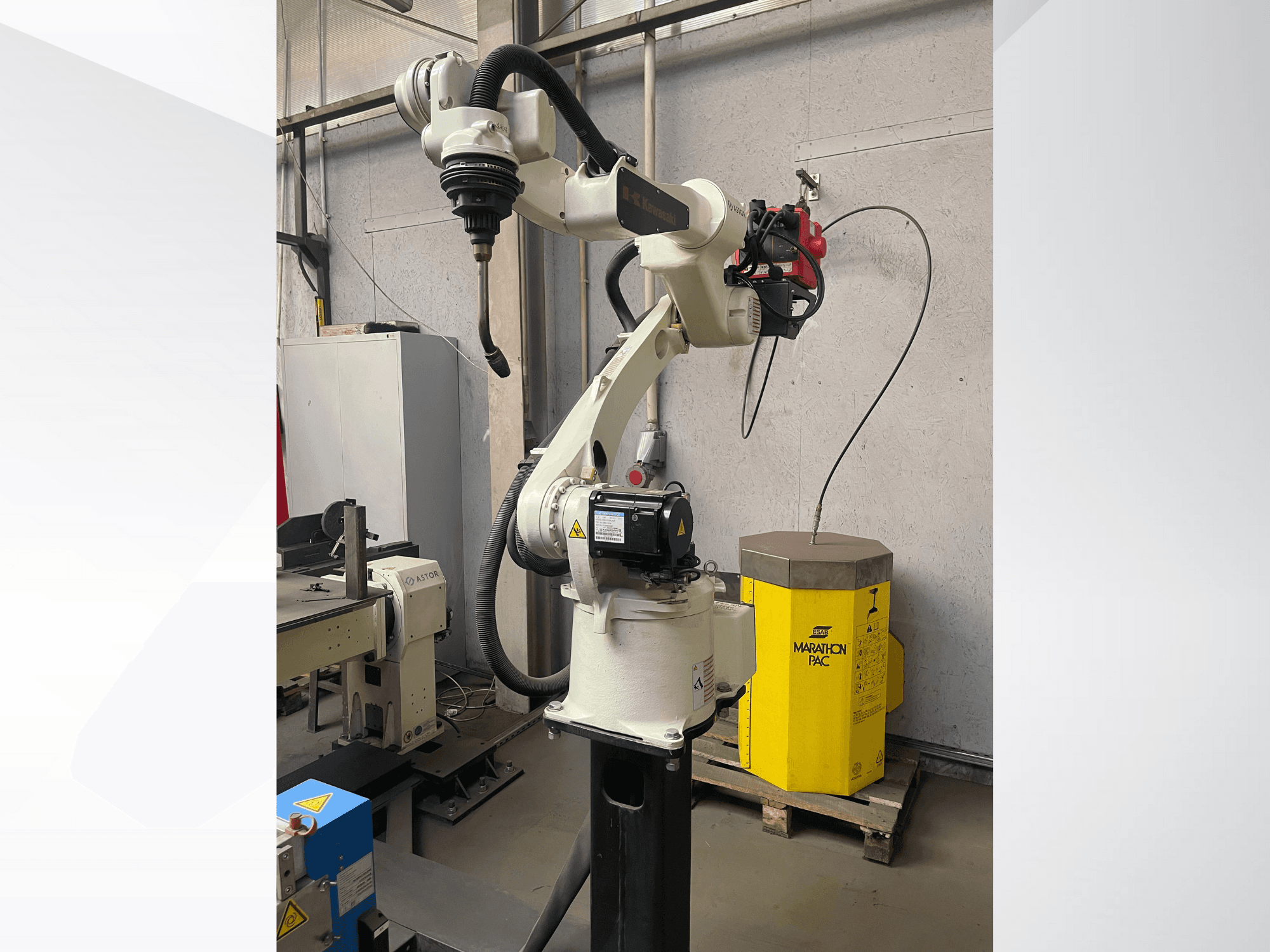 Роботизированная рука Kawasaki с видом сбоку, с установленным держателем инструмента, на заднем плане желтый силовой агрегат.