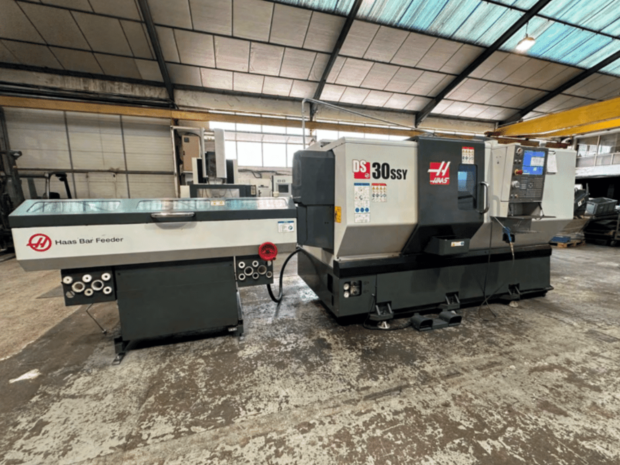 Токарный станок с ЧПУ Haas DS-30SSY с устройством подачи прутка Haas, вид сбоку, демонстрирующий панель управления и механизм подачи в условиях мастерской.