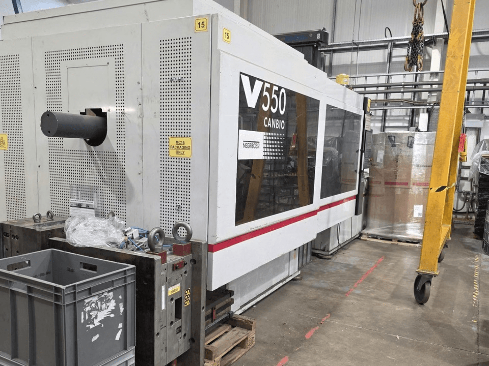 Гидравлическая машина для литья под давлением Negri Bossi V55000H-4250, вид сбоку, панель управления и серые ящики на переднем плане.