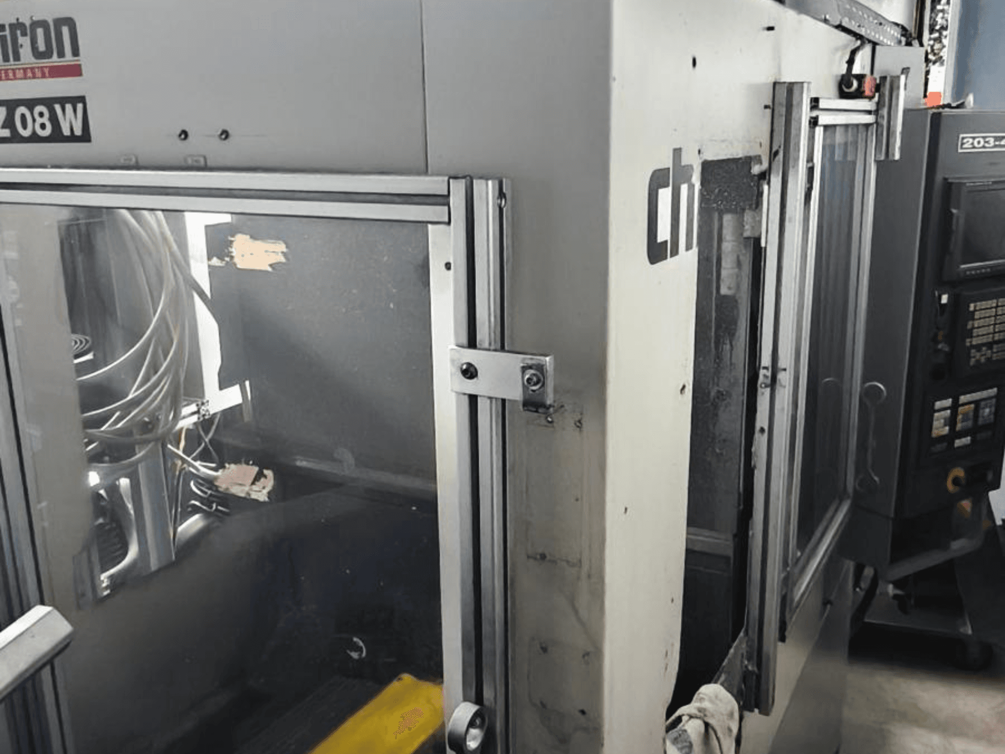 Вертикальный обрабатывающий центр CHIRON FZ 08 W, вид спереди с изображением панели управления и частично открытых дверей, с видимыми внутренними компонентами.