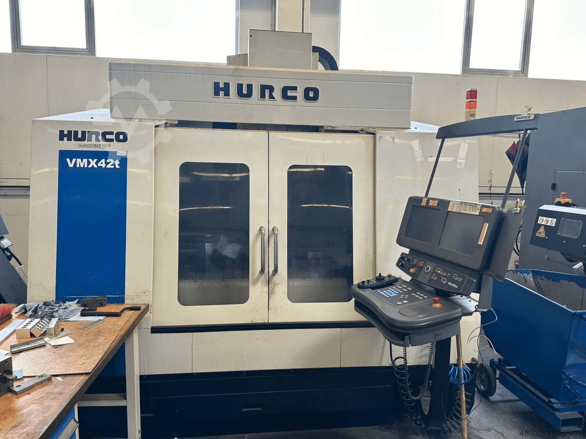 Вертикальный обрабатывающий центр Hurco VMX42t, вид спереди, на котором видны панель управления и внутреннее пространство с заготовками и инструментами.