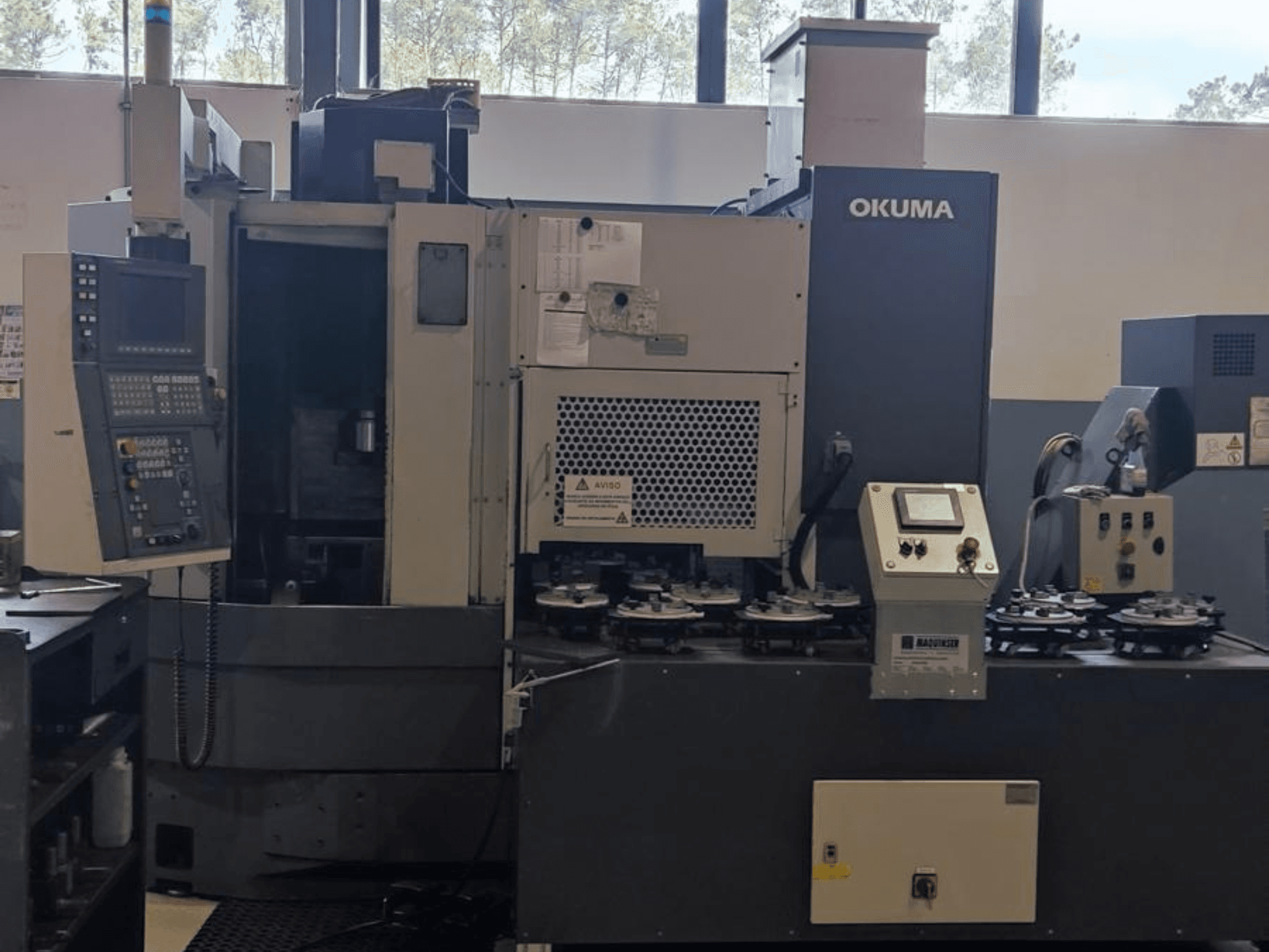 Вертикальный токарный станок Okuma LVT300 с видом спереди, панель управления, держатели инструмента и зона обработки.