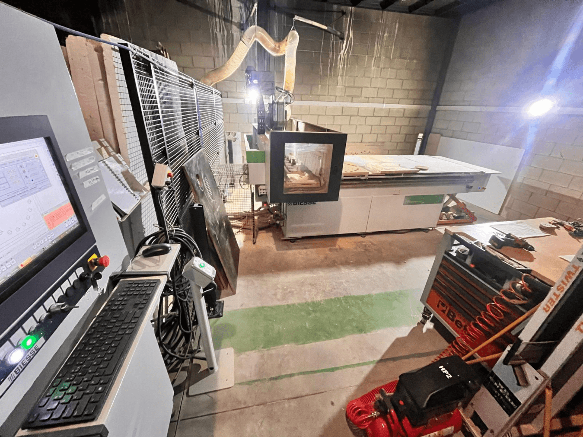 Станок с ЧПУ Biesse в мастерской, вид сбоку на панель управления, пылеудаление, инструменты и различные материалы на столе.