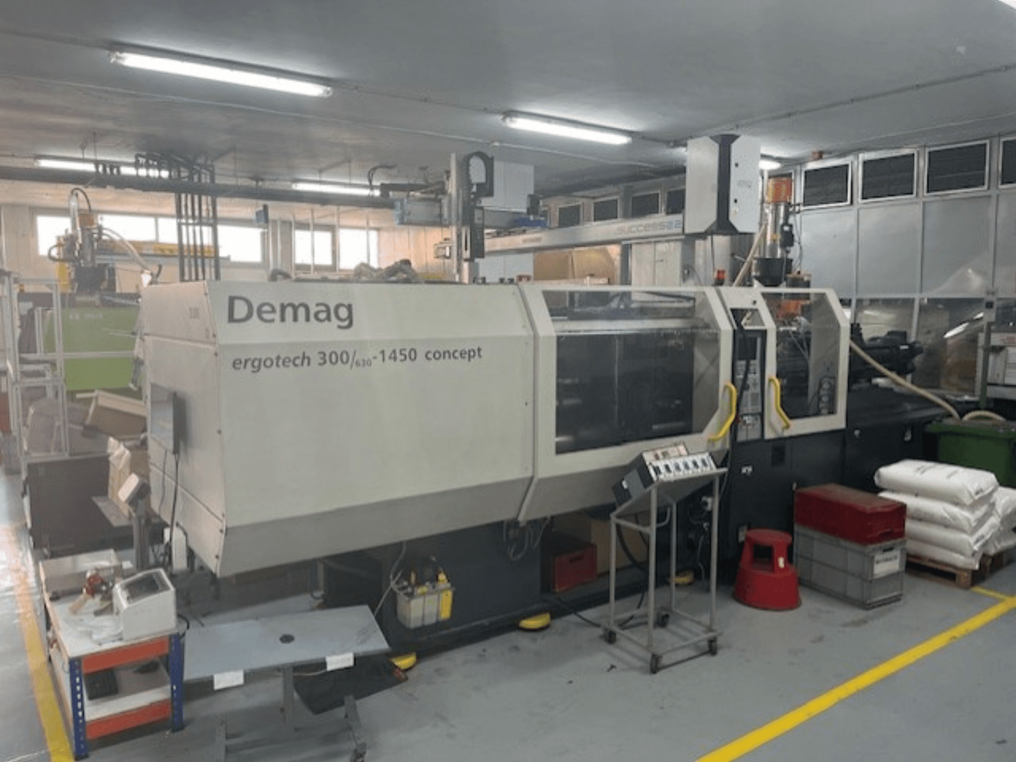 Гидравлическая машина для литья под давлением Demag ERGOTECH CONCEPT 3000-1450, вид спереди, с органами управления и материалами рядом.