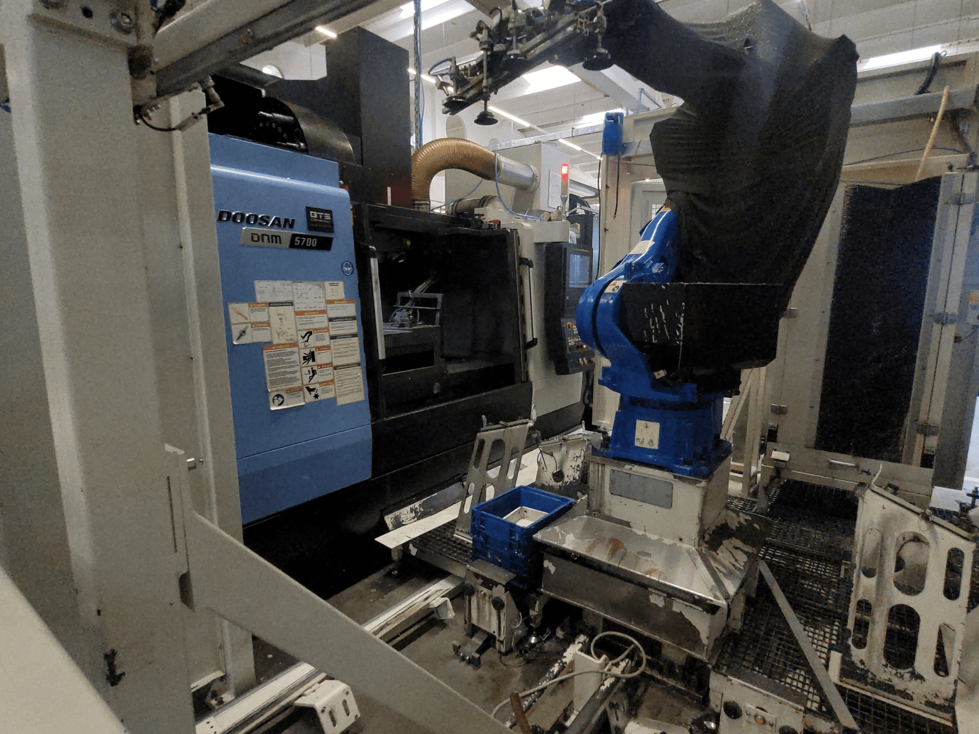 Вертикальный обрабатывающий центр DOOSAN DNM 5700 в заводской обстановке: вид спереди и интеграция с роботом-манипулятором.