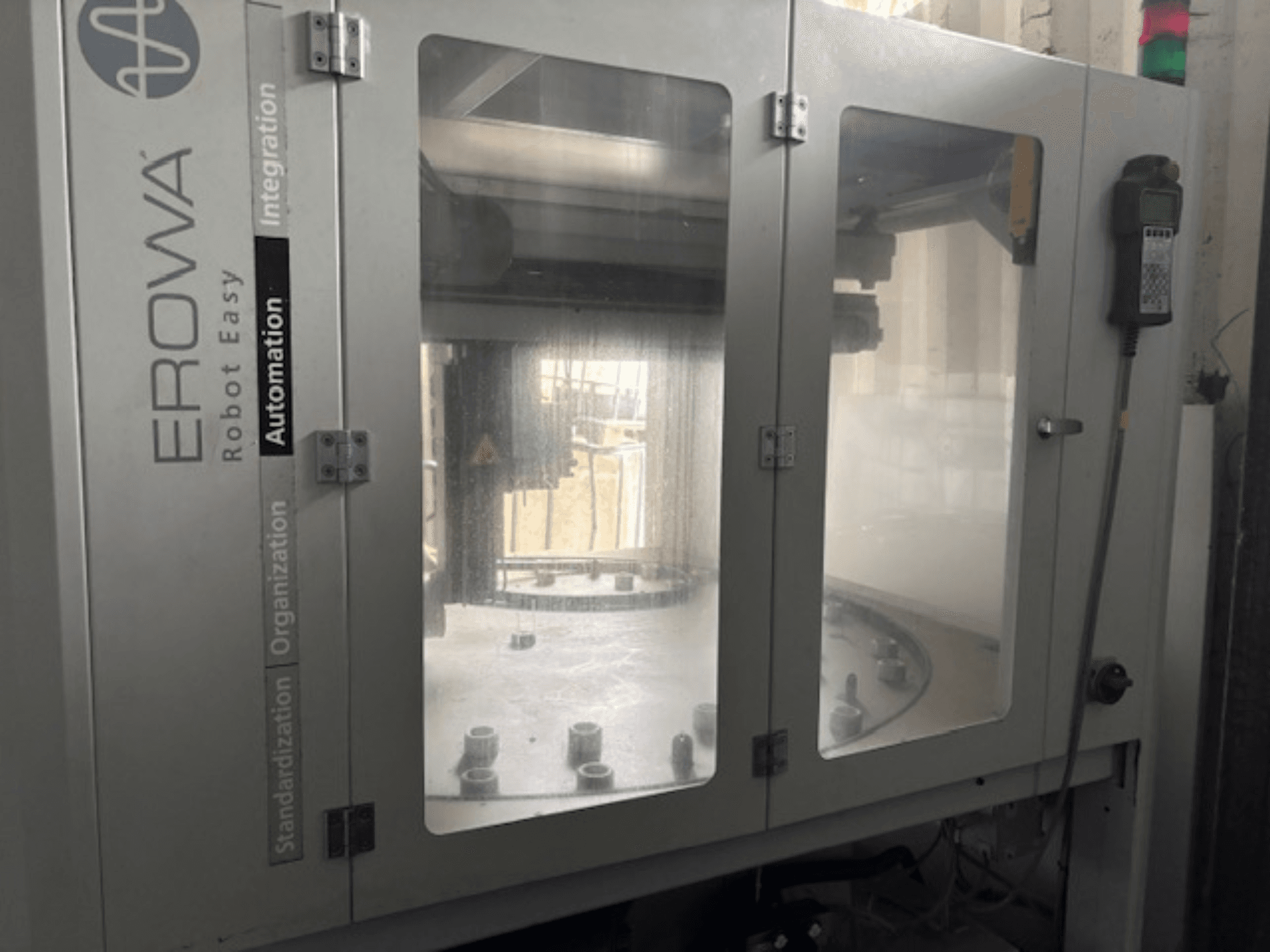 Вид спереди EROWA Robot Easy Automation; прозрачные двери, видимые компоненты автоматизации и панель управления.