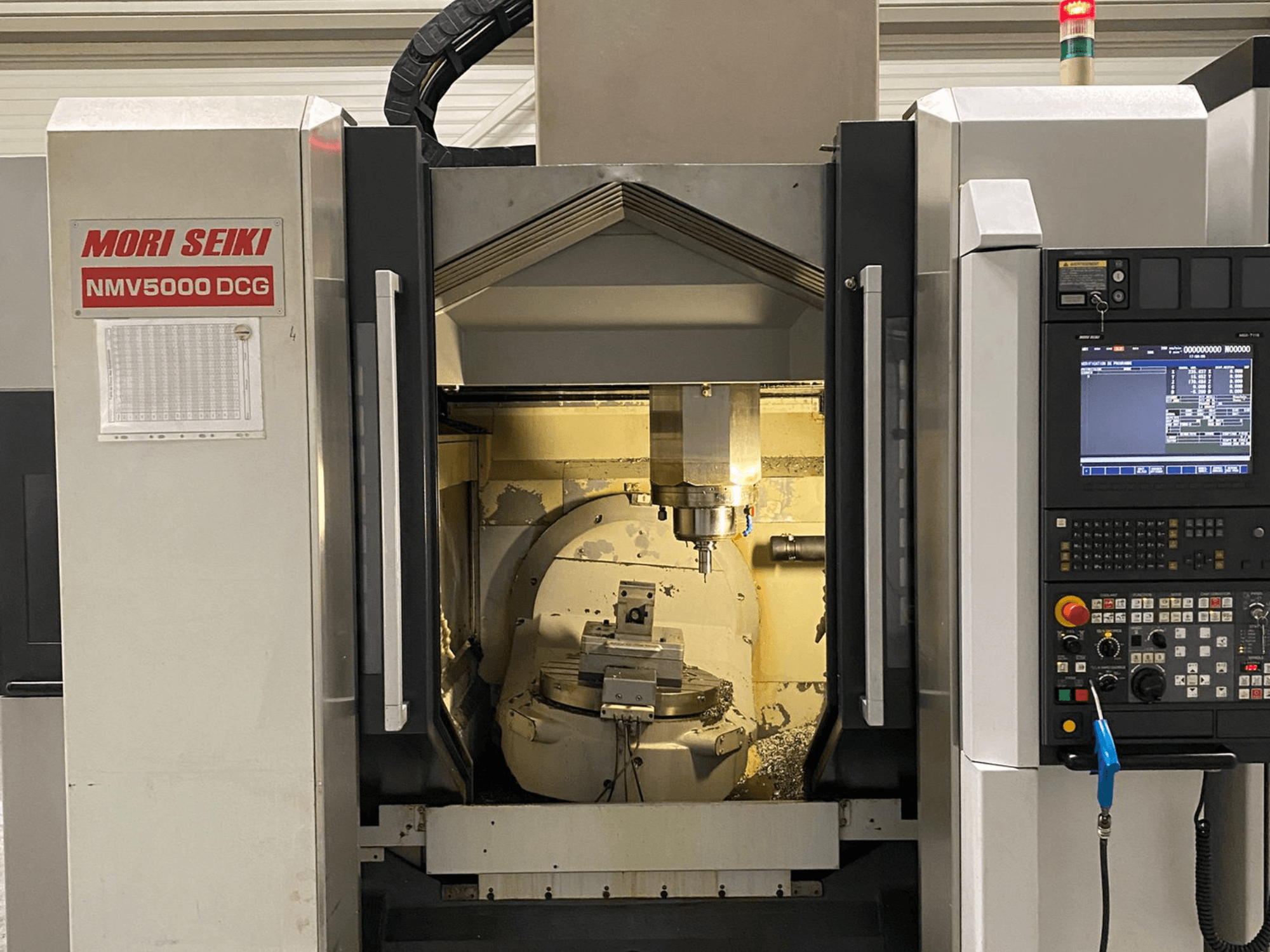 Универсальный обрабатывающий центр MORI SEIKI NMV 5000DCG, вид спереди, показывающий панель управления и внутреннюю зону обработки.