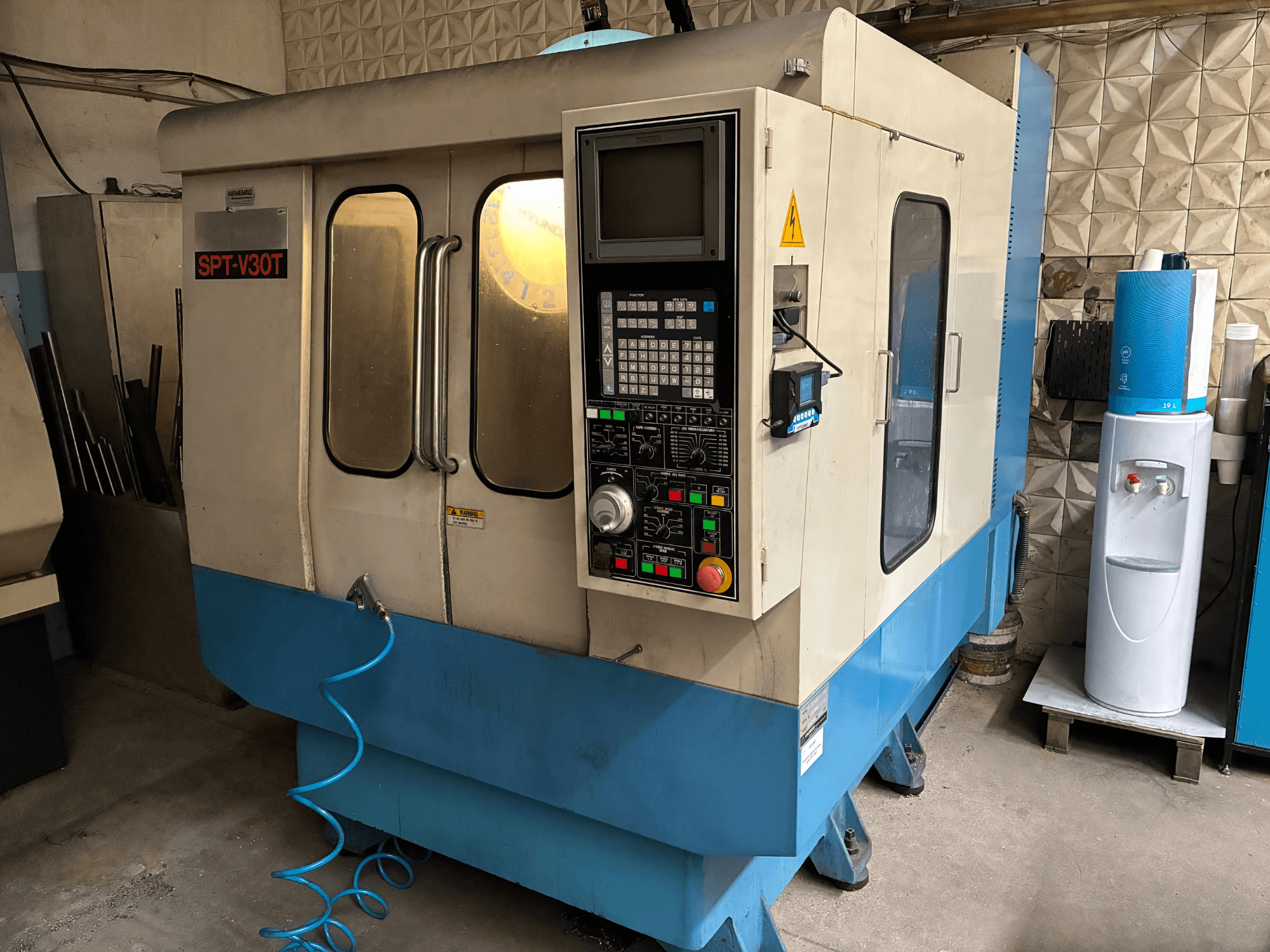 Станок с ЧПУ SPT-V30T сине-белого цвета, вид спереди с панелью управления, дверцами и воздушным шлангом. Идеально подходит для точной обработки.