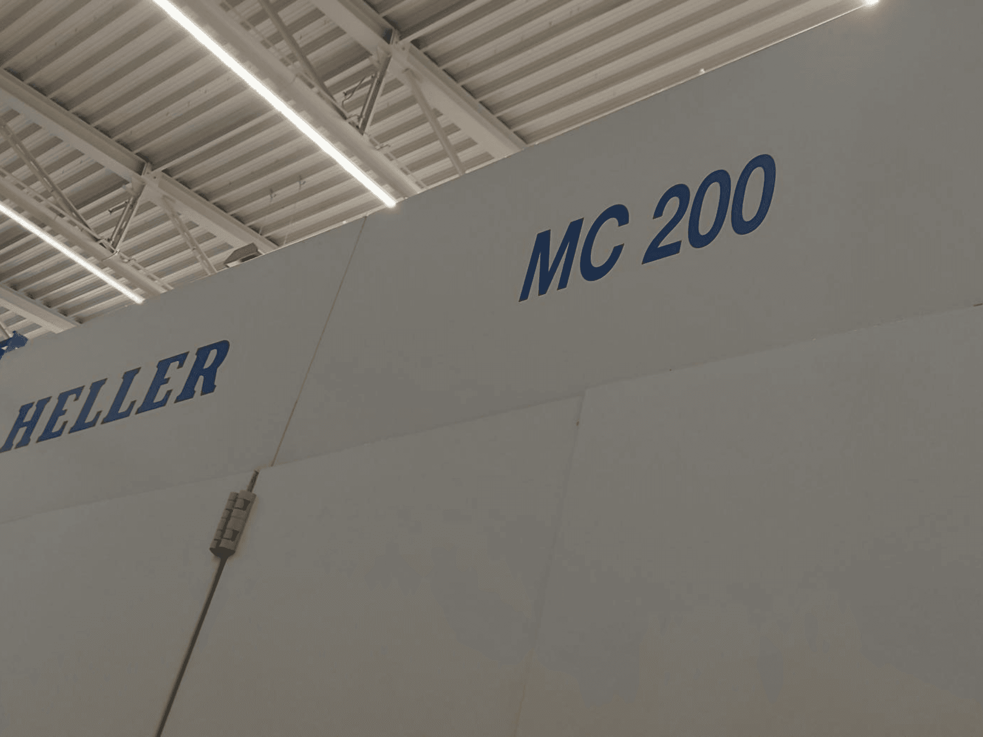 Горизонтальный обрабатывающий центр Heller MC 200, показан сбоку, марка и модель выделены синими буквами на белой поверхности.