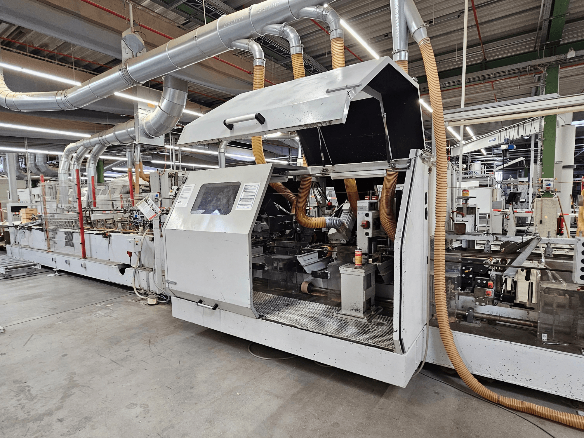Кромкооблицовочный станок HOMAG FG63 в заводских условиях, вид сбоку, демонстрирующий рабочие узлы и систему пылеудаления.