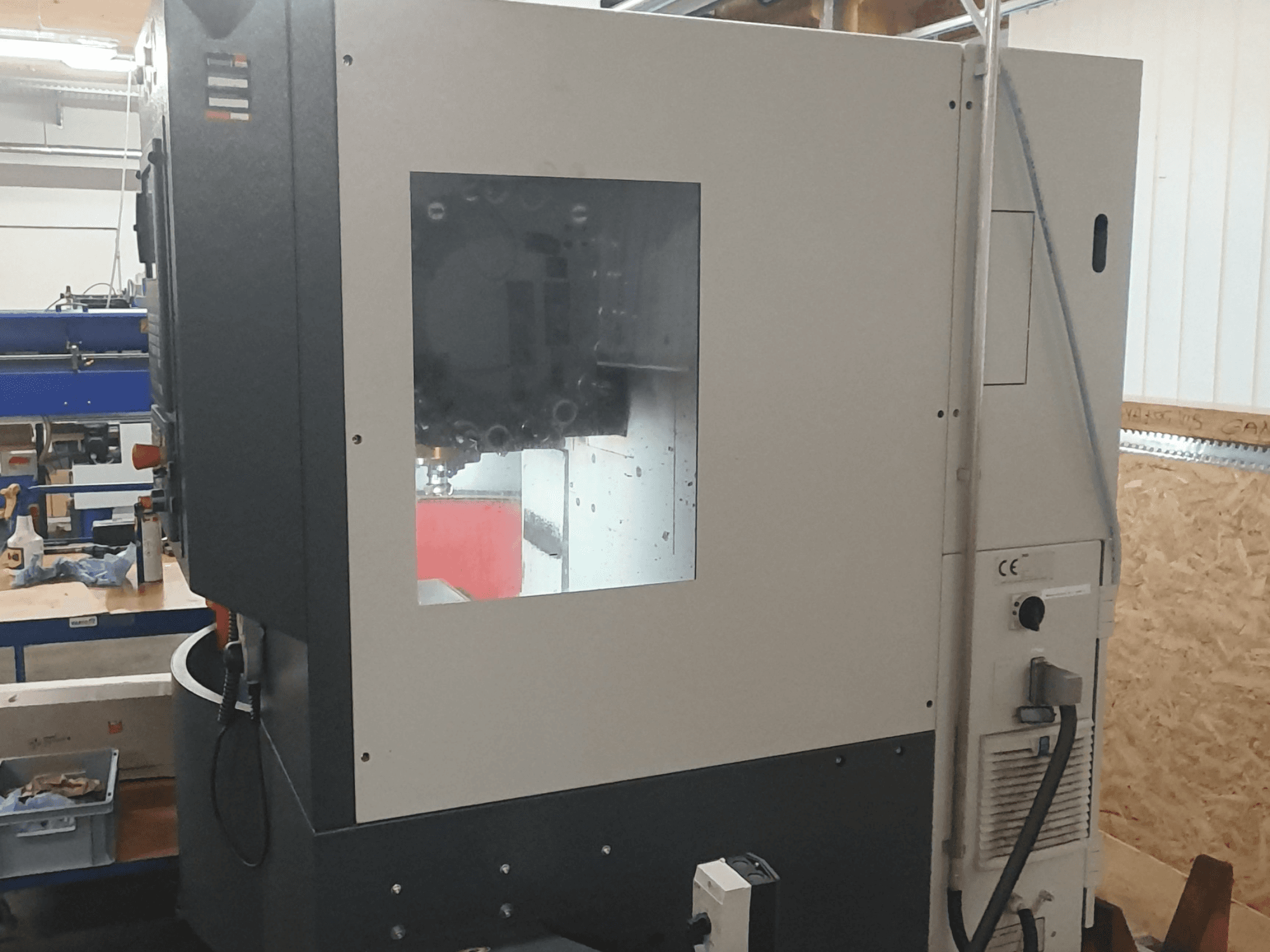 Вид сбоку на металлообрабатывающий станок с видимой панелью управления, большим смотровым окном и сложными внутренними компонентами.