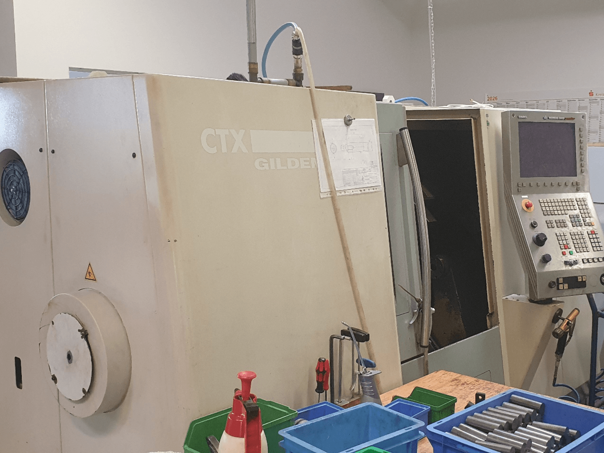 Вид спереди на горизонтальный токарный станок DMG GILDEMEISTER CTX 310; видна панель управления, на переднем плане — инструменты и контейнеры.