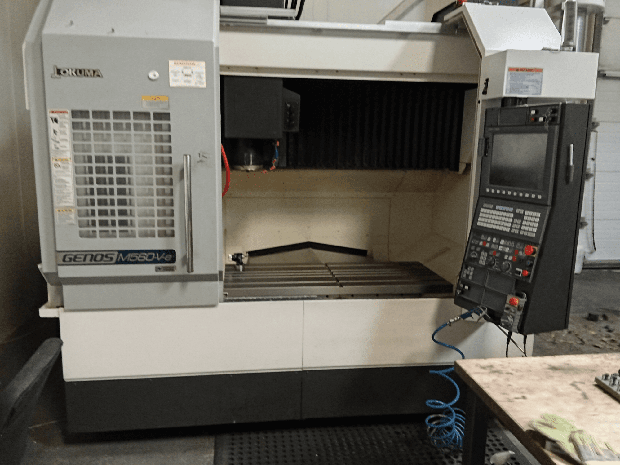 Okuma GENOS M560-V, вид спереди вертикального обрабатывающего центра с панелью управления, интерфейсом ЧПУ и видимой зоной резки.