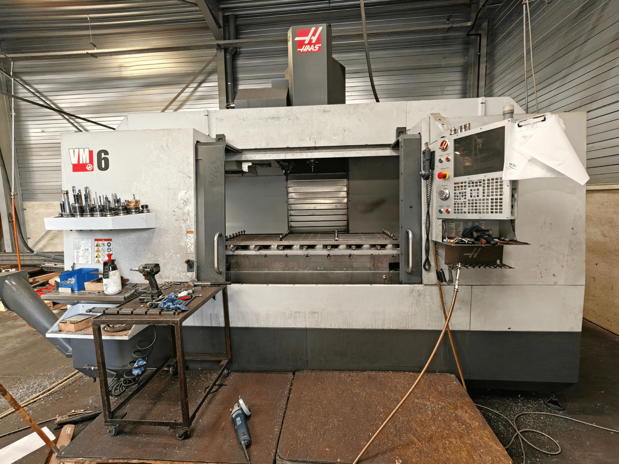 Вертикальный обрабатывающий центр Haas VM-6, вид спереди, на котором видны хранилище инструментов, панель управления и мусор в рабочей зоне.