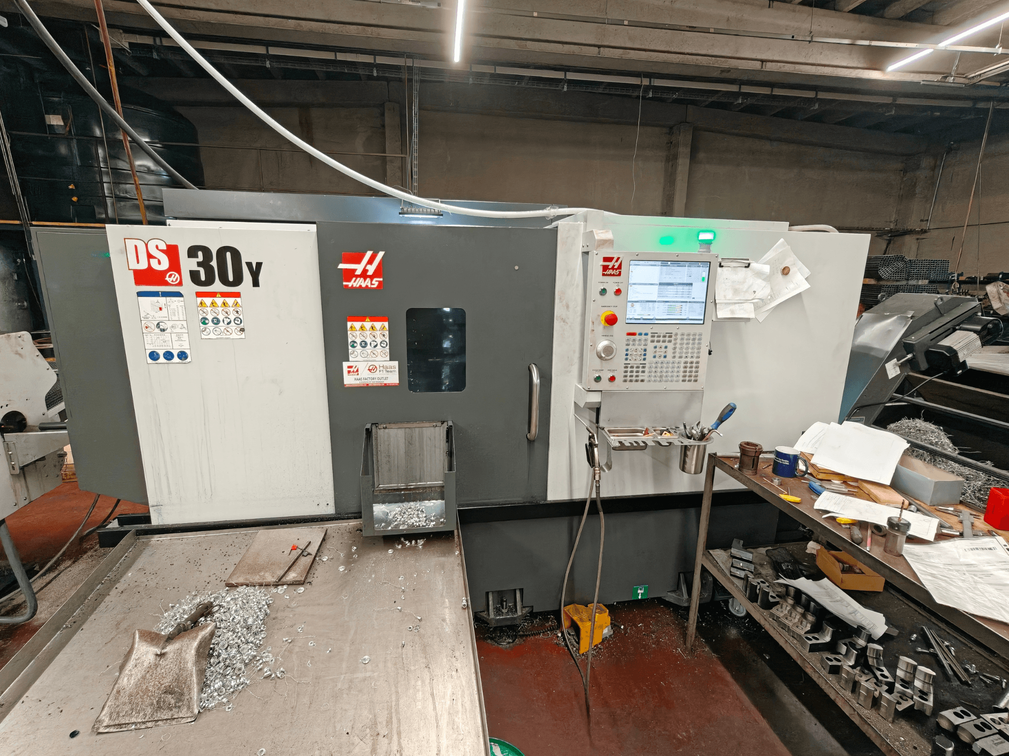Горизонтальный токарный станок HAAS DS30Y в цехе, вид спереди, на котором видны панель управления и металлическая стружка на поверхности.