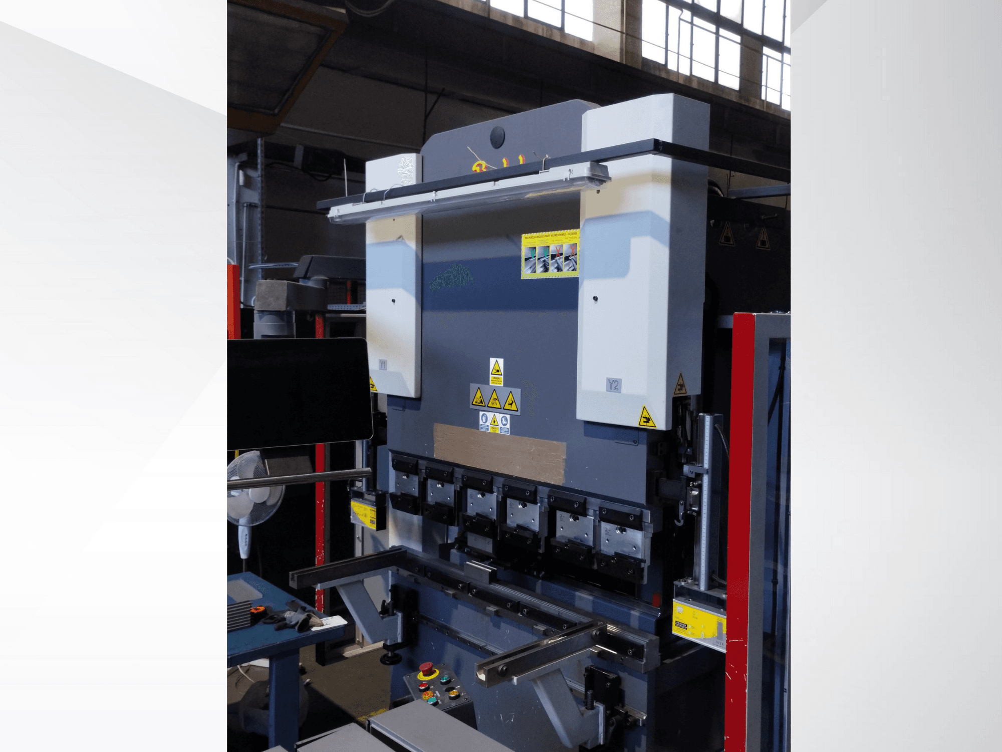 Листогибочный станок, вид спереди. Имеет видимые элементы управления, наклейки безопасности и несколько держателей штампов для точной гибки.