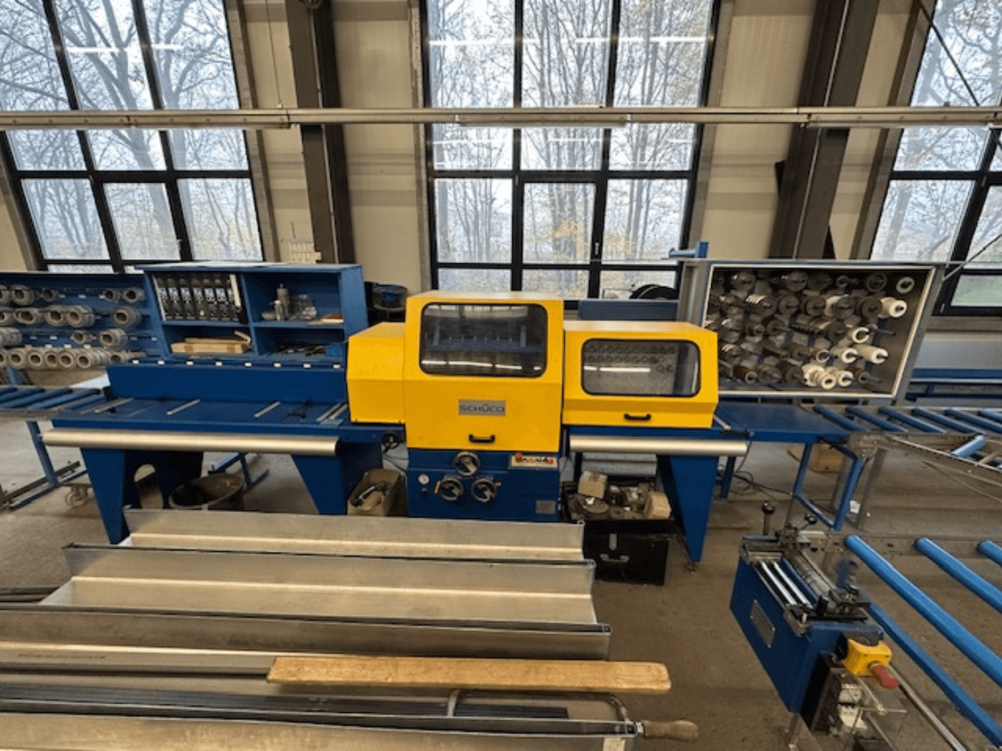 Вид спереди станка SCHÜCO ISOMAT 4 с желтой панелью управления, несколькими валиками и отсеком для хранения.