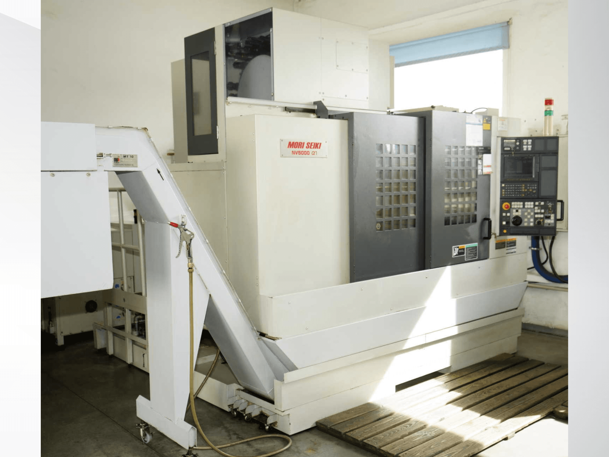 Вертикальный обрабатывающий центр MORI SEIKI NV 5000 alpha1 в виде спереди, на котором видны панель управления, средства безопасности и зона загрузки.