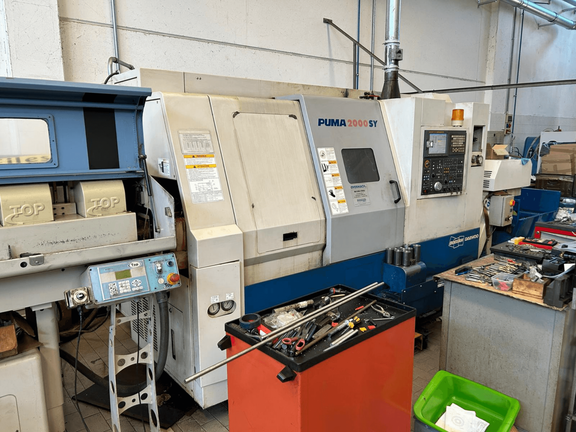 Горизонтальный токарный станок DOOSAN PUMA 2000SY в цехе, вид сбоку, на котором видны панель управления и инструменты, расположенные рядом.