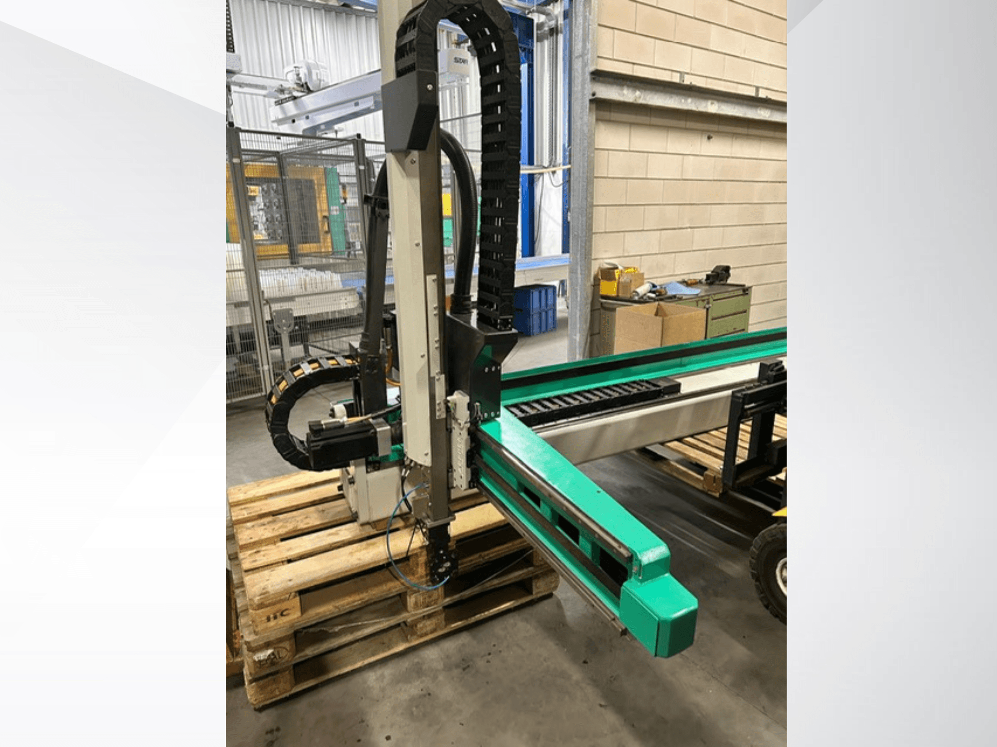 Arburg Multilift Select 15kg quer, вид сбоку на систему перемещения заготовок на деревянных поддонах, с изображением роботизированной руки и компонентов управления.