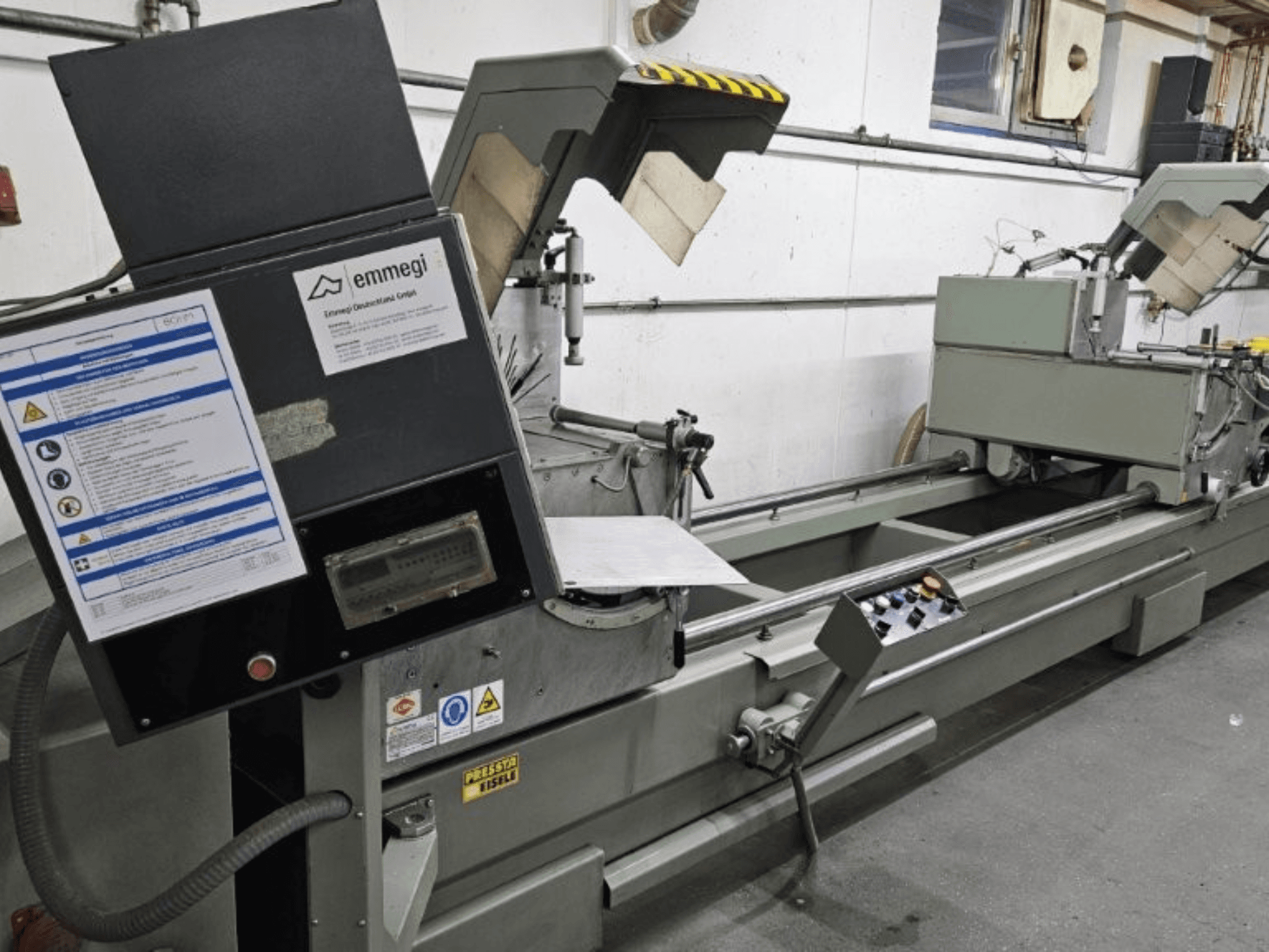 Промышленная машина для резки Emmegi, вид спереди, панель управления, защитные наклейки и рабочие элементы.