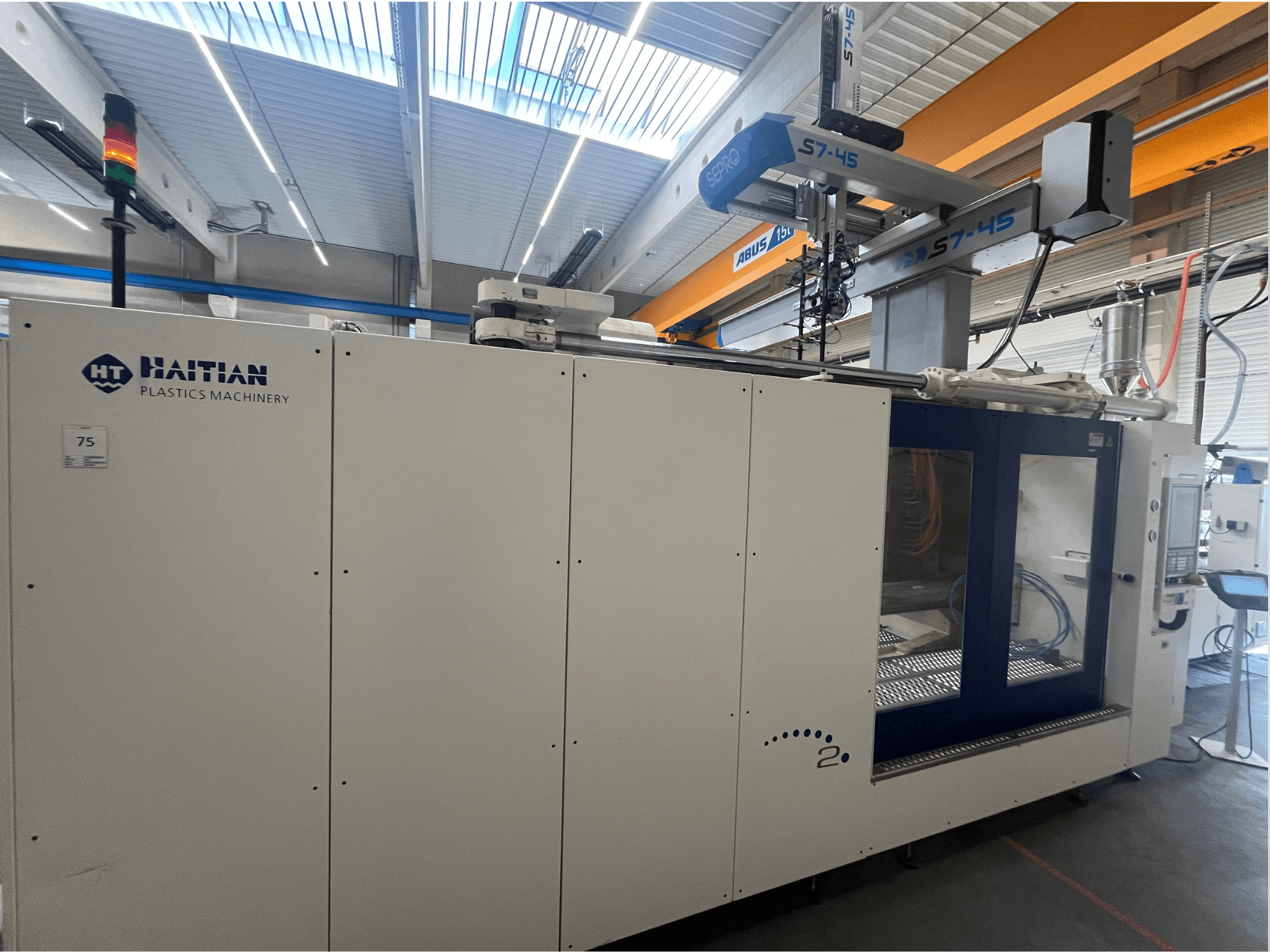 Термопластавтомат Haitian S7-45 в боковом разрезе с панелью управления и световым индикатором безопасности. Бело-голубой дизайн.