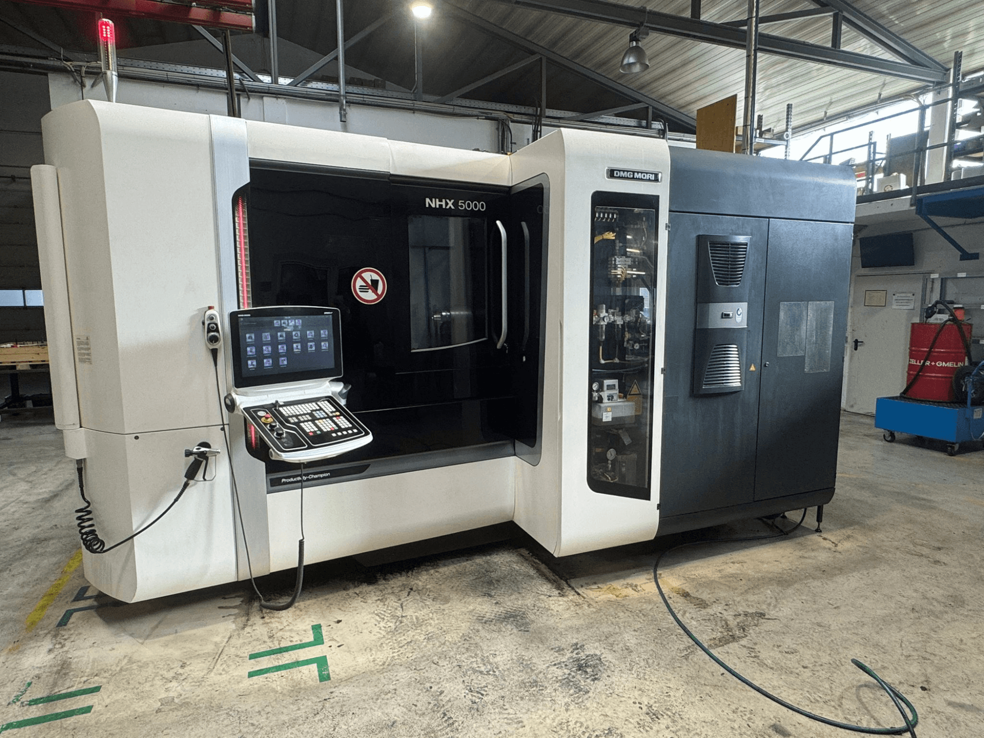 Горизонтальный обрабатывающий центр DMG MORI NHX 5000, вид спереди, видна панель управления и индикаторы безопасности.