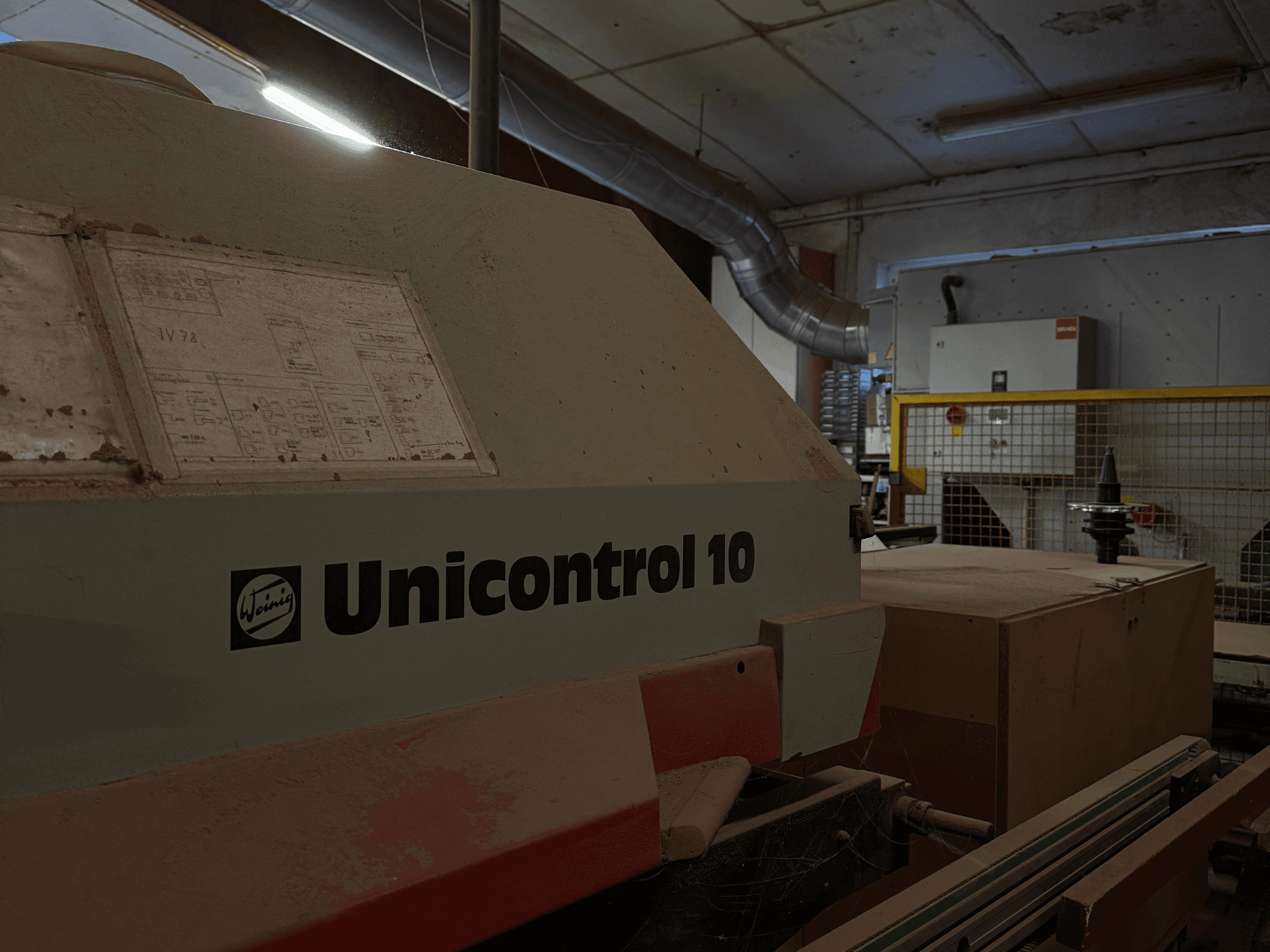 Станок Weinig Unicontrol 10, вид сбоку, пыльная поверхность, на передней панели видны технические схемы.