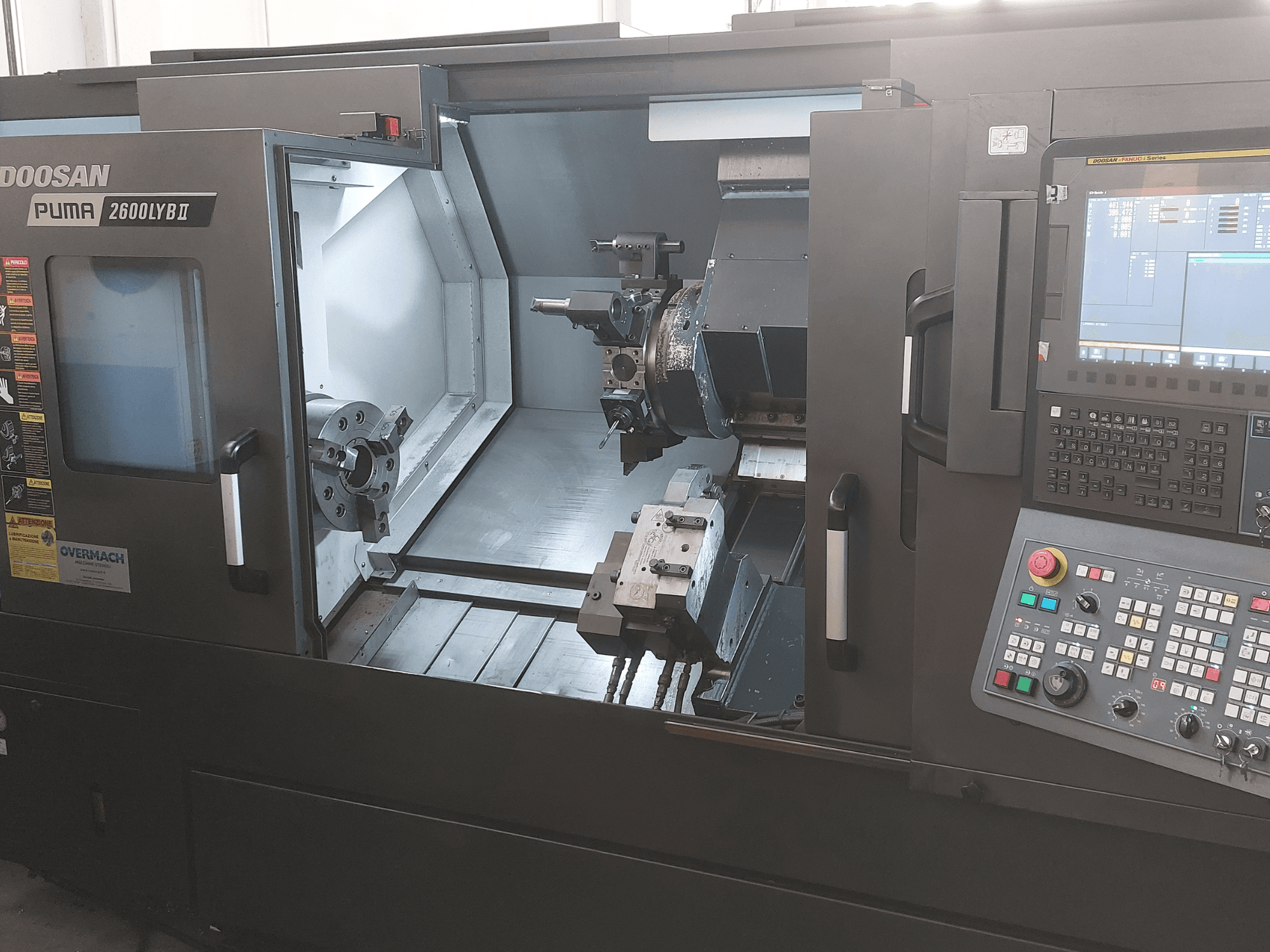 Горизонтальный токарный станок DOOSAN Puma 2600 LYB II на виде спереди, демонстрирует внутреннюю часть с патроном, держателем инструмента и панелью управления.