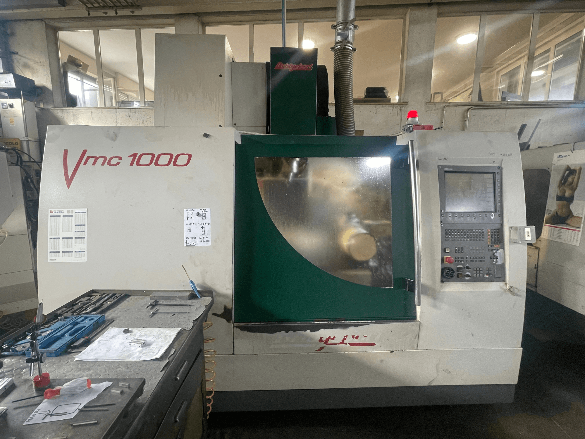 Вертикальный обрабатывающий центр Bridgeport VMC 1000/30, вид спереди, на котором видны панель управления и основной корпус, а рядом — инструменты.