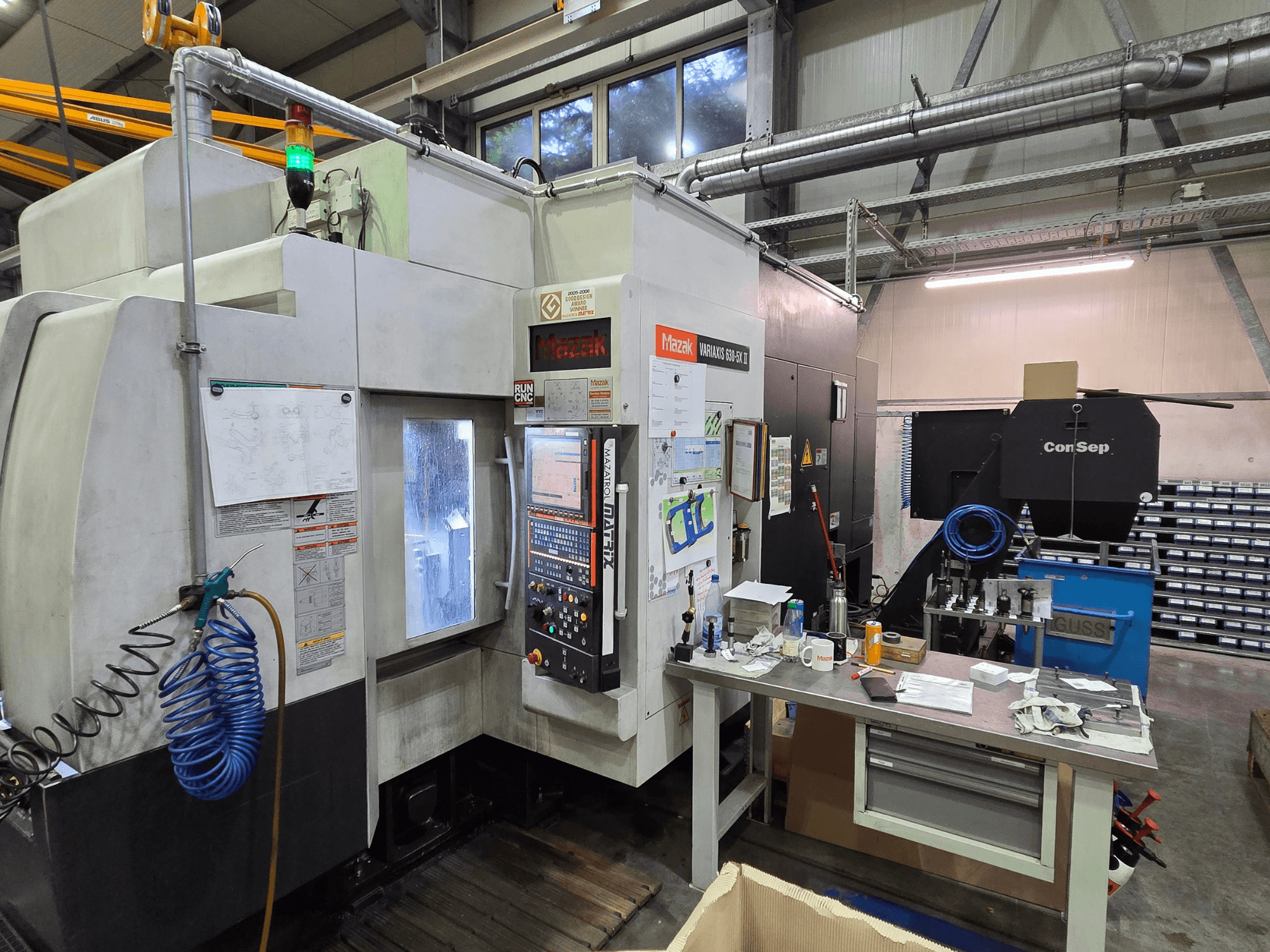 Станок с ЧПУ Mazak Variaxis 630-5X в мастерской, вид спереди с панелью управления, шлангом и принадлежностями на боковом столе.
