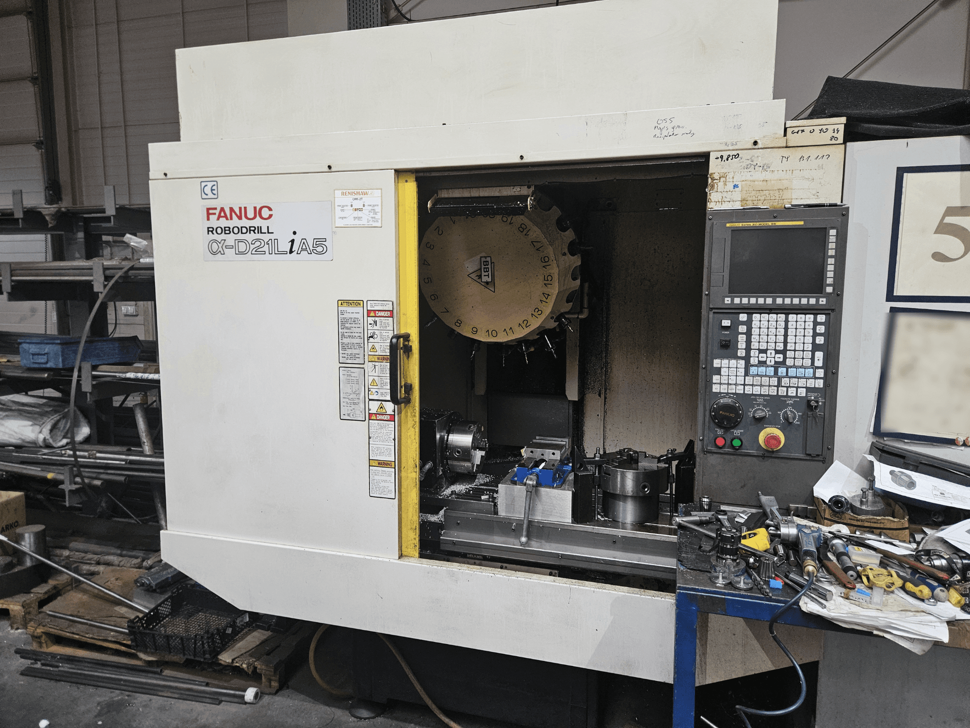 Рободрель FANUC Robodrill α-D21LiA5, вид спереди на держатель инструмента и панель управления, в окружении инструментов и оборудования в мастерской.